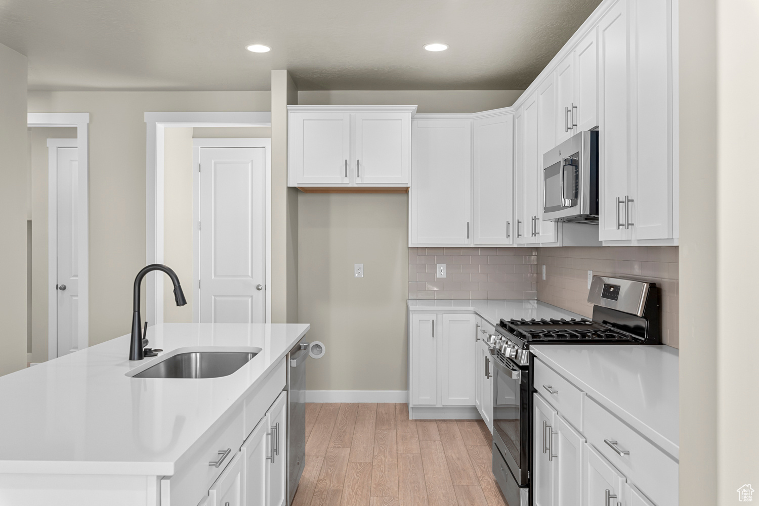 Kitchen with sink, white cabinets, appliances with stainless steel finishes, and light wood-type flooring
