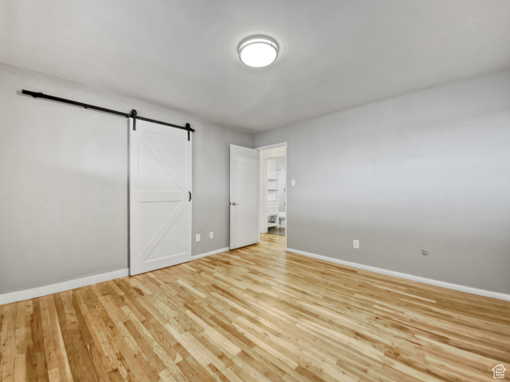 Unfurnished bedroom with a barn door and light hardwood / wood-style floors