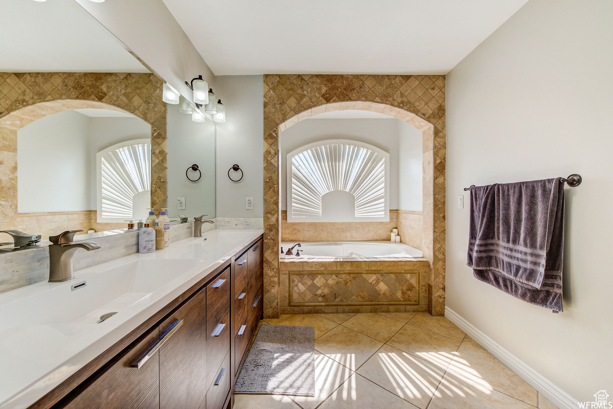 Bathroom with dual bowl vanity, tile floors, and a relaxing tiled bath
