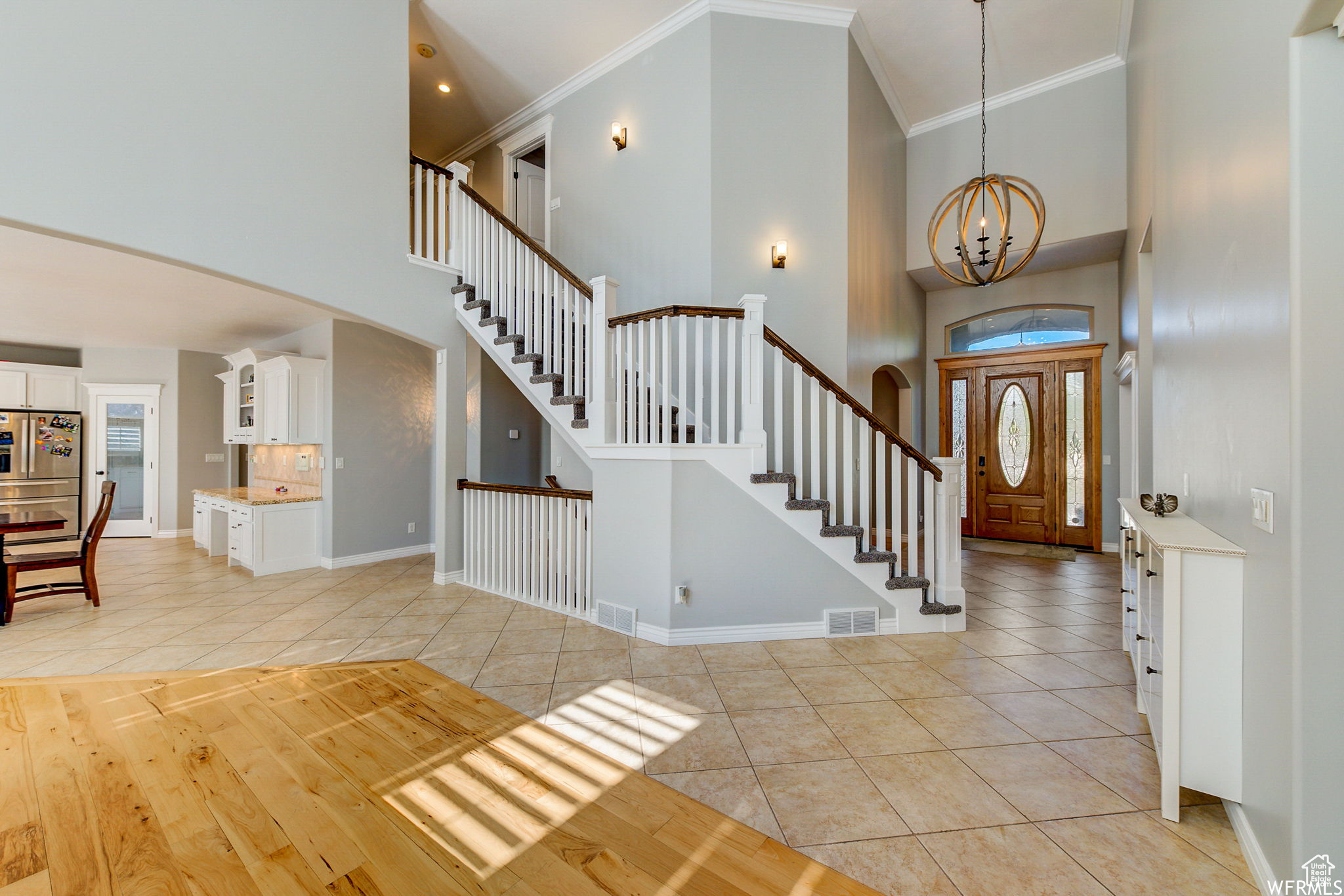 Tiled entrance foyer with an inviting chandelier, ornamental molding, and a towering ceiling