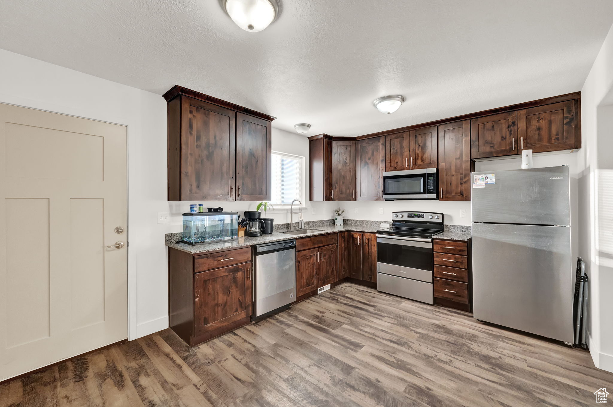 Kitchen featuring sink, appliances with stainless steel finishes, light stone counters, and light hardwood / wood-style flooring