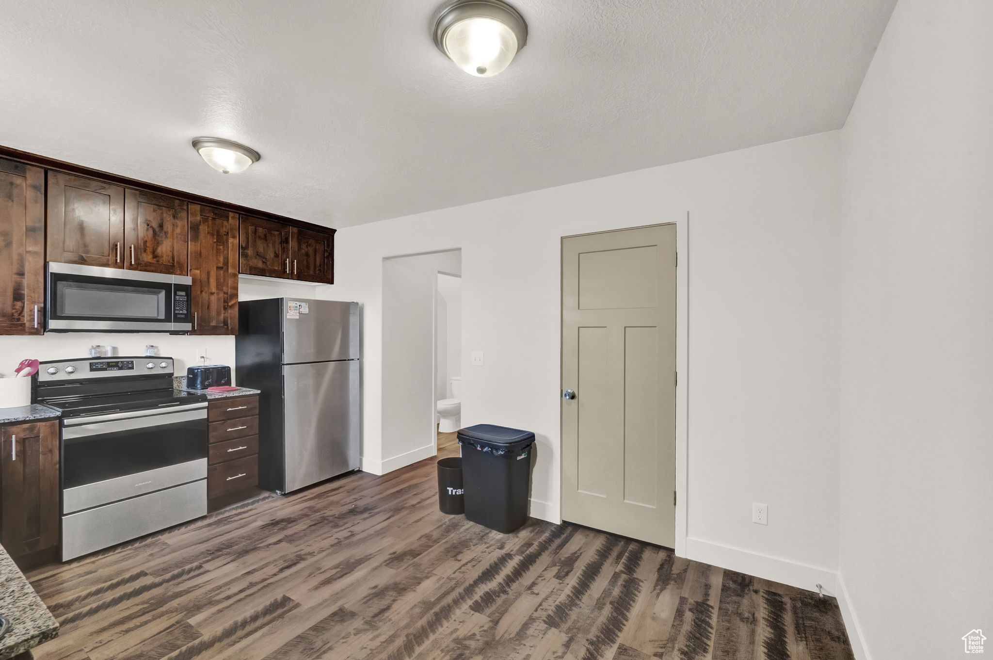 Kitchen with dark hardwood / wood-style floors, dark brown cabinetry, and stainless steel appliances