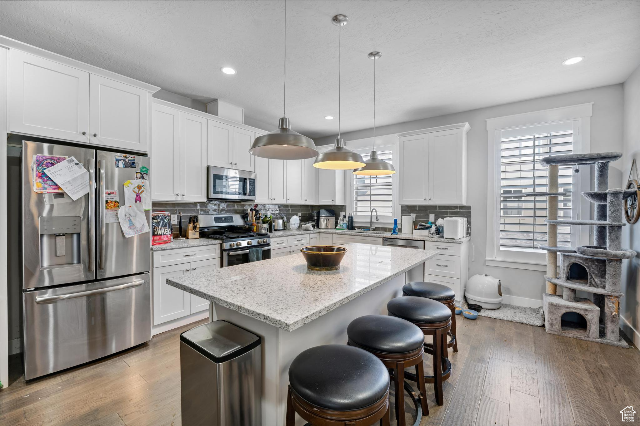 Kitchen featuring a kitchen island, light wood-type flooring, tasteful backsplash, decorative light fixtures, and appliances with stainless steel finishes