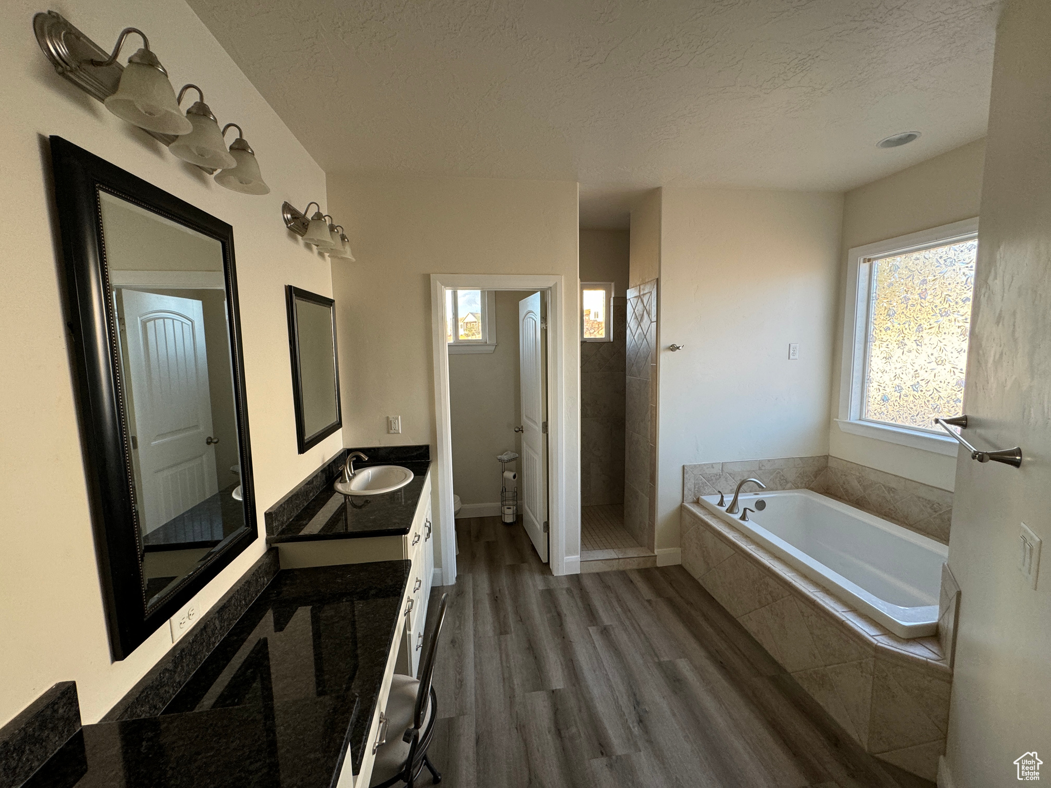 Master Bathroom featuring hardwood / wood-style flooring, a relaxing tiled bath, a textured ceiling, and vanity with extensive cabinet space