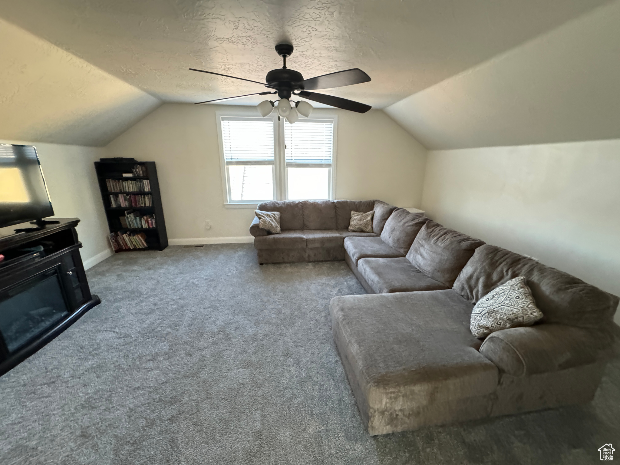Living room featuring vaulted ceiling, ceiling fan, a textured ceiling, and carpet flooring