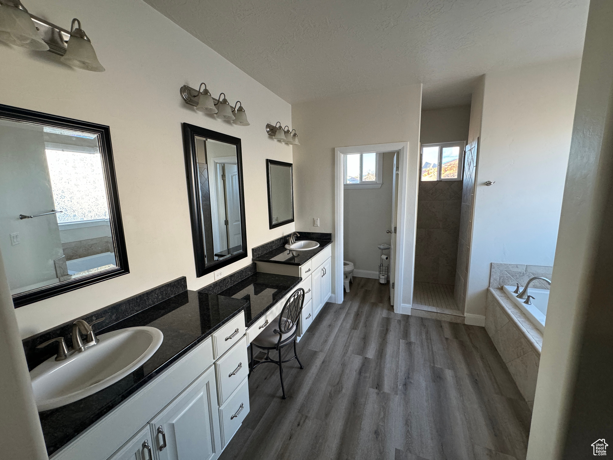 Master Bathroom with toilet, hardwood / wood-style floors, double vanity, and tiled bath