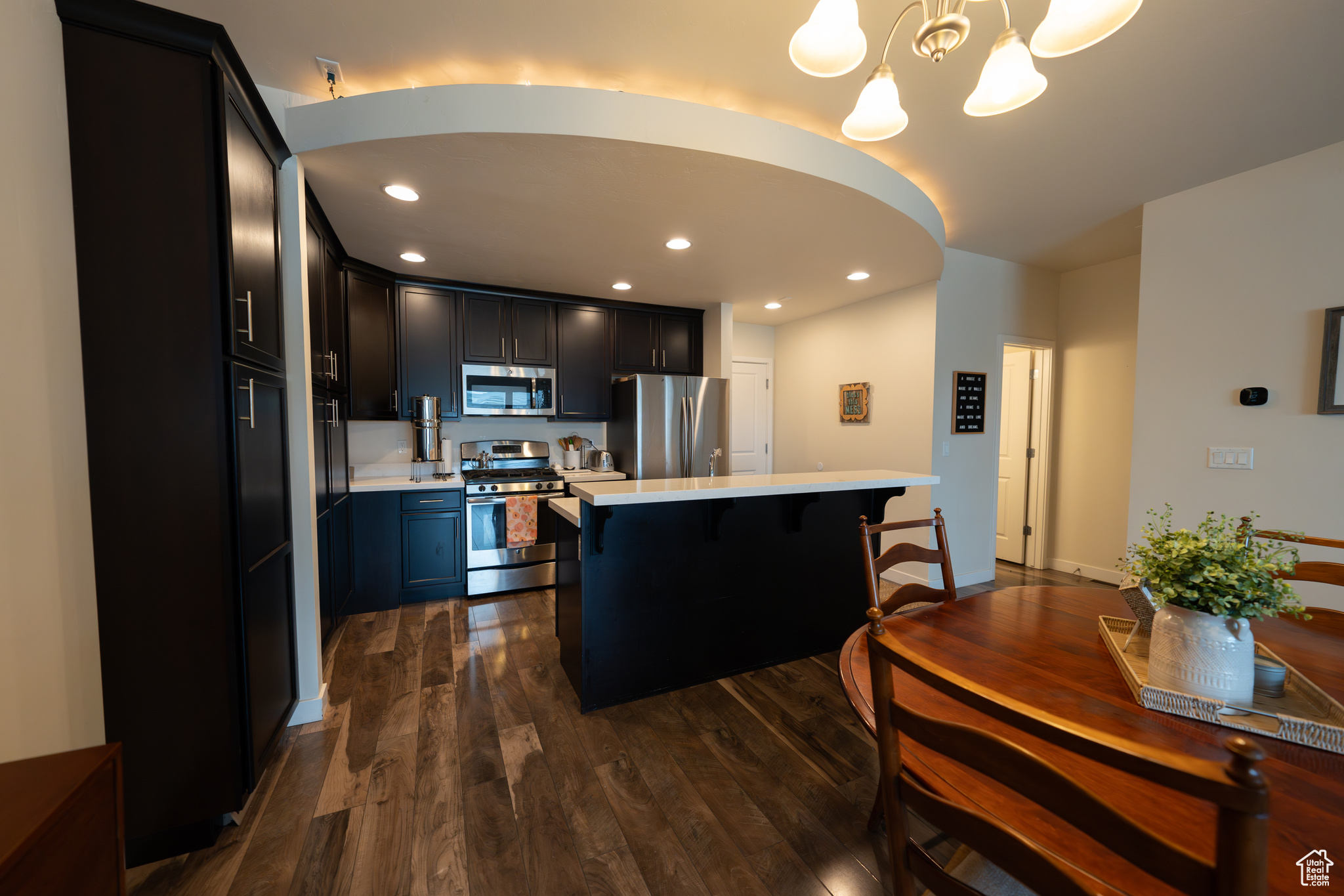 Kitchen with pendant lighting, a chandelier, a breakfast bar, appliances with stainless steel finishes, and dark hardwood / wood-style floors