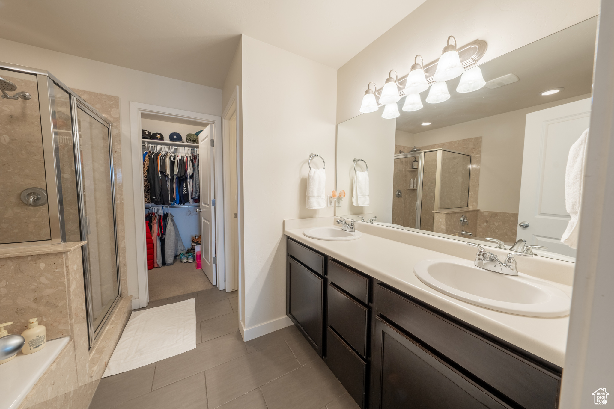 Bathroom featuring a shower with door, dual sinks, tile flooring, and vanity with extensive cabinet space