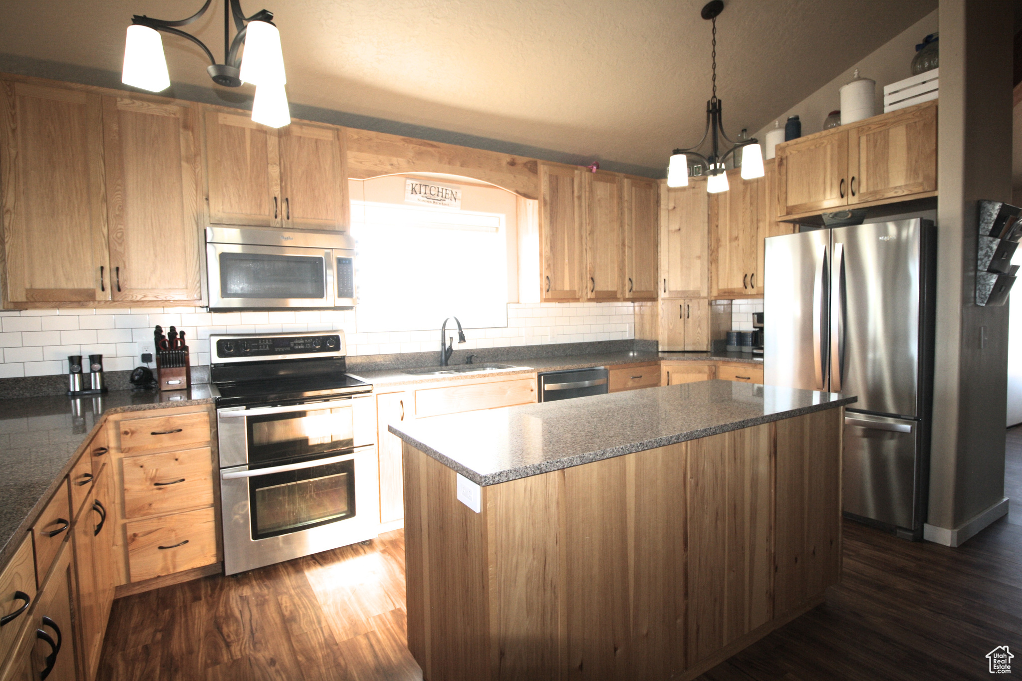 Kitchen featuring pendant lighting, dark hardwood / wood-style flooring, stainless steel appliances, a kitchen island, and sink