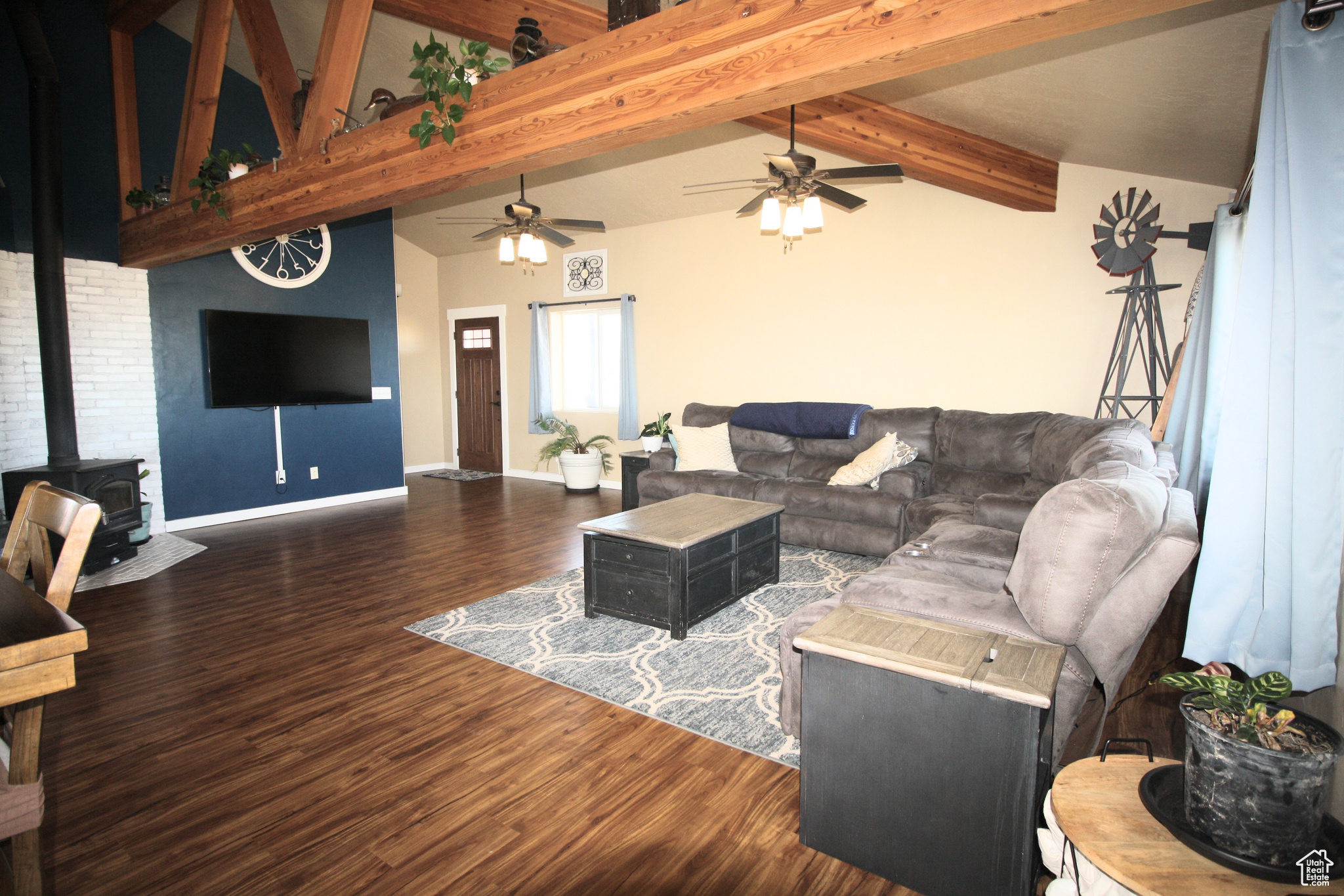 Living room with dark hardwood / wood-style flooring, a high ceiling, a wood stove, beam ceiling, and ceiling fan