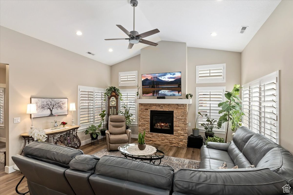 Living room featuring a stone fireplace, ceiling fan, and high vaulted ceiling