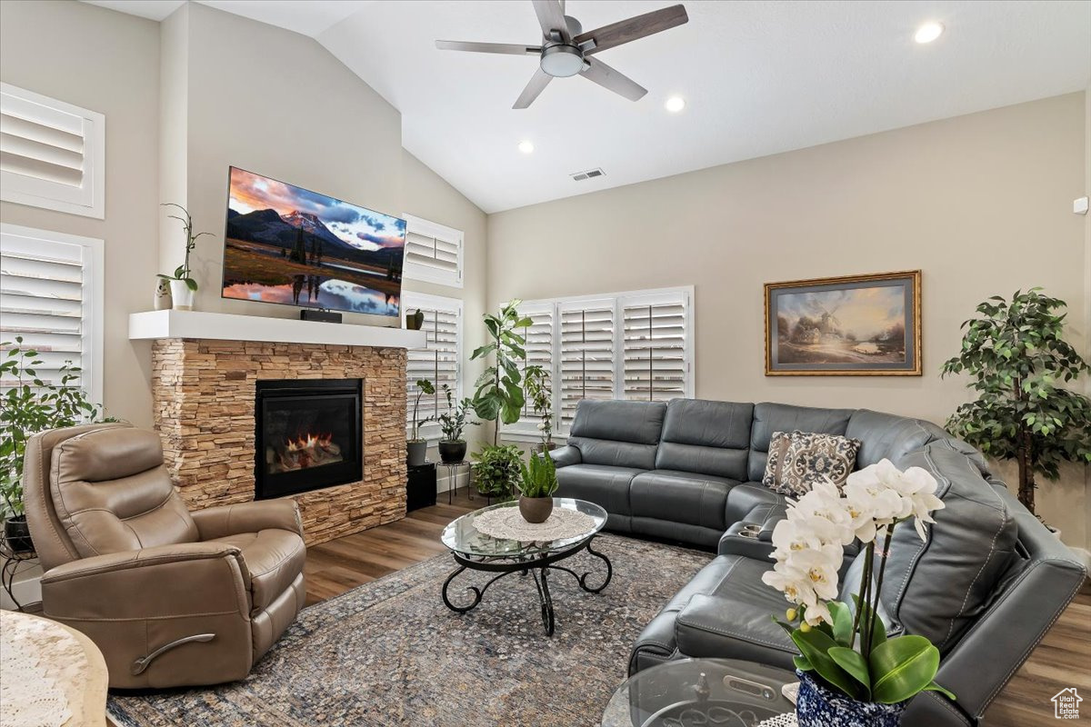 Living room featuring high vaulted ceiling, ceiling fan, and a stone fireplace