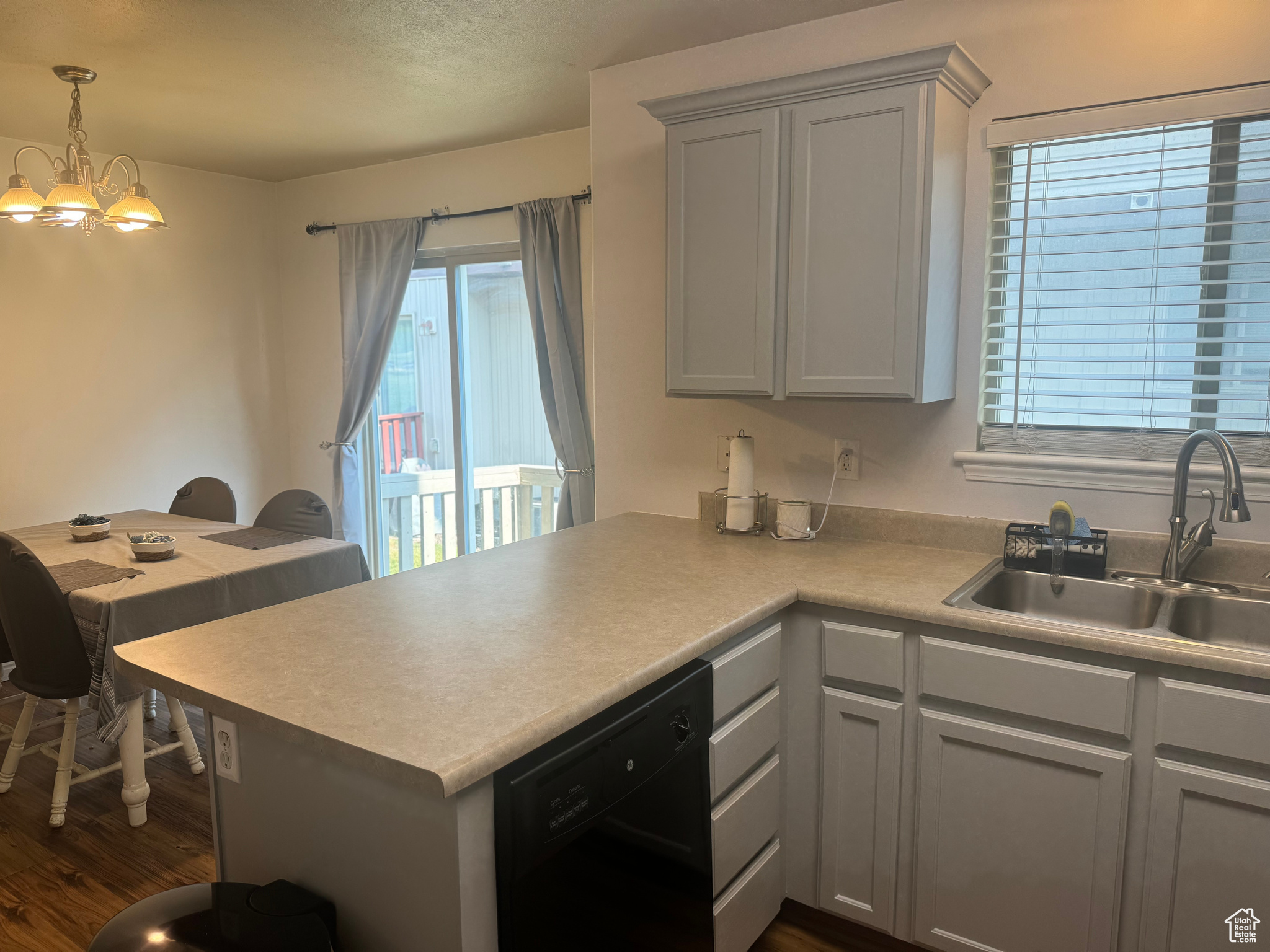 Kitchen featuring black dishwasher, sink, a chandelier, kitchen peninsula, and LVP wood-style flooring