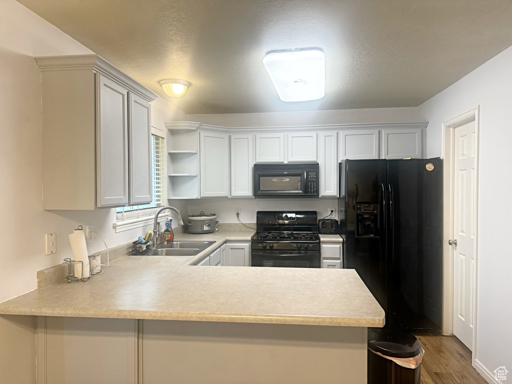 Kitchen featuring black appliances, light grey cabinetry, LVP wood-type flooring, and kitchen peninsula