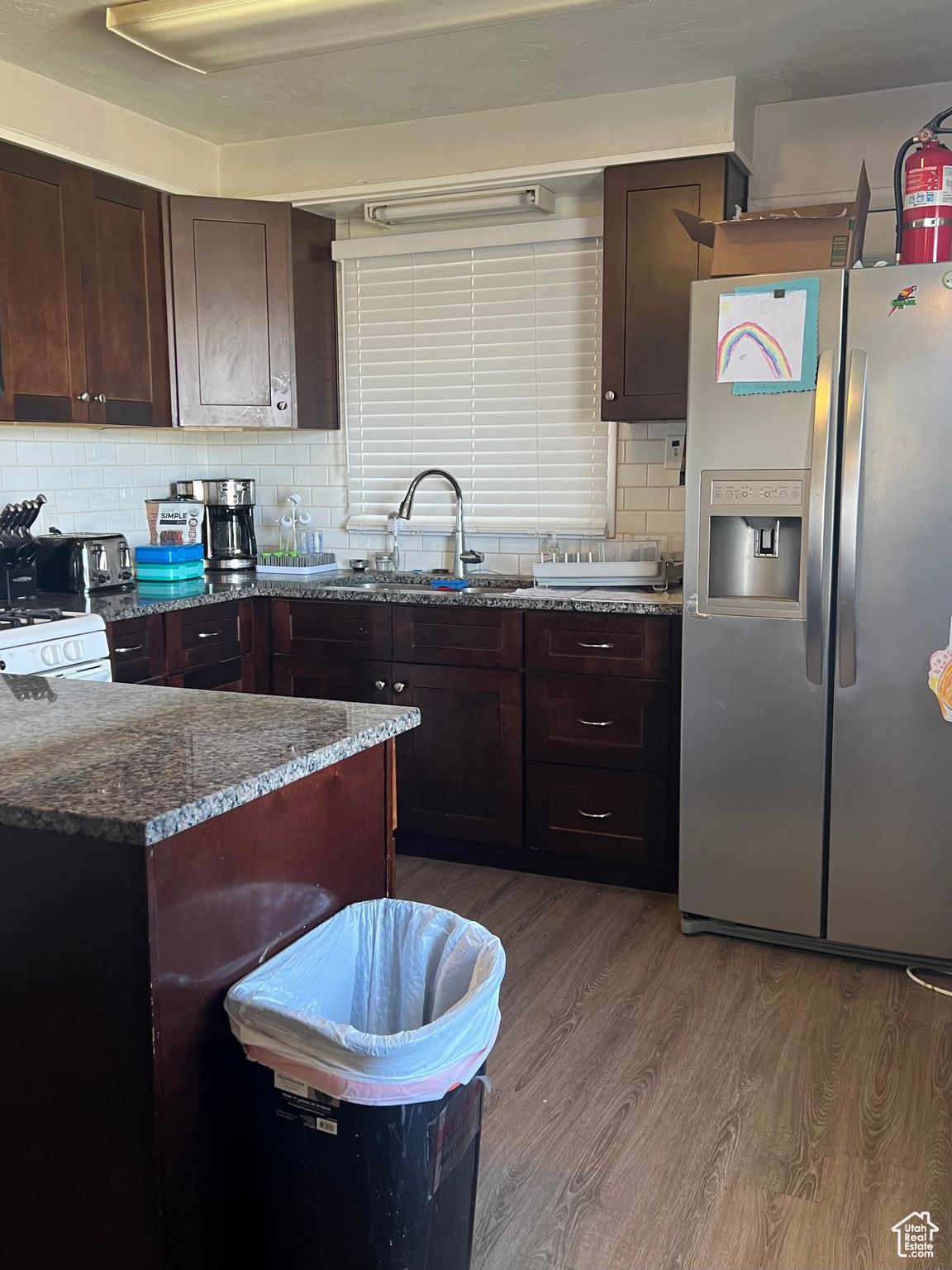 Kitchen featuring hardwood / wood-style flooring, stainless steel fridge, tasteful backsplash, dark stone counters, and sink