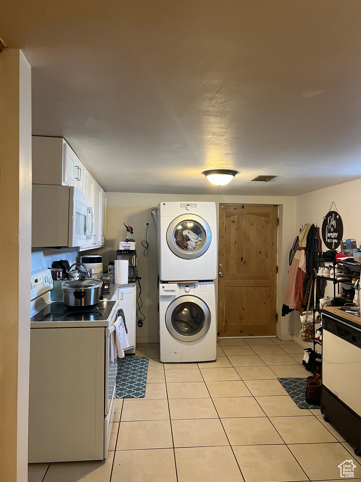 Kitchen with dishwashing machine, electric range oven, white cabinets, stacked washer / dryer, and light tile floors