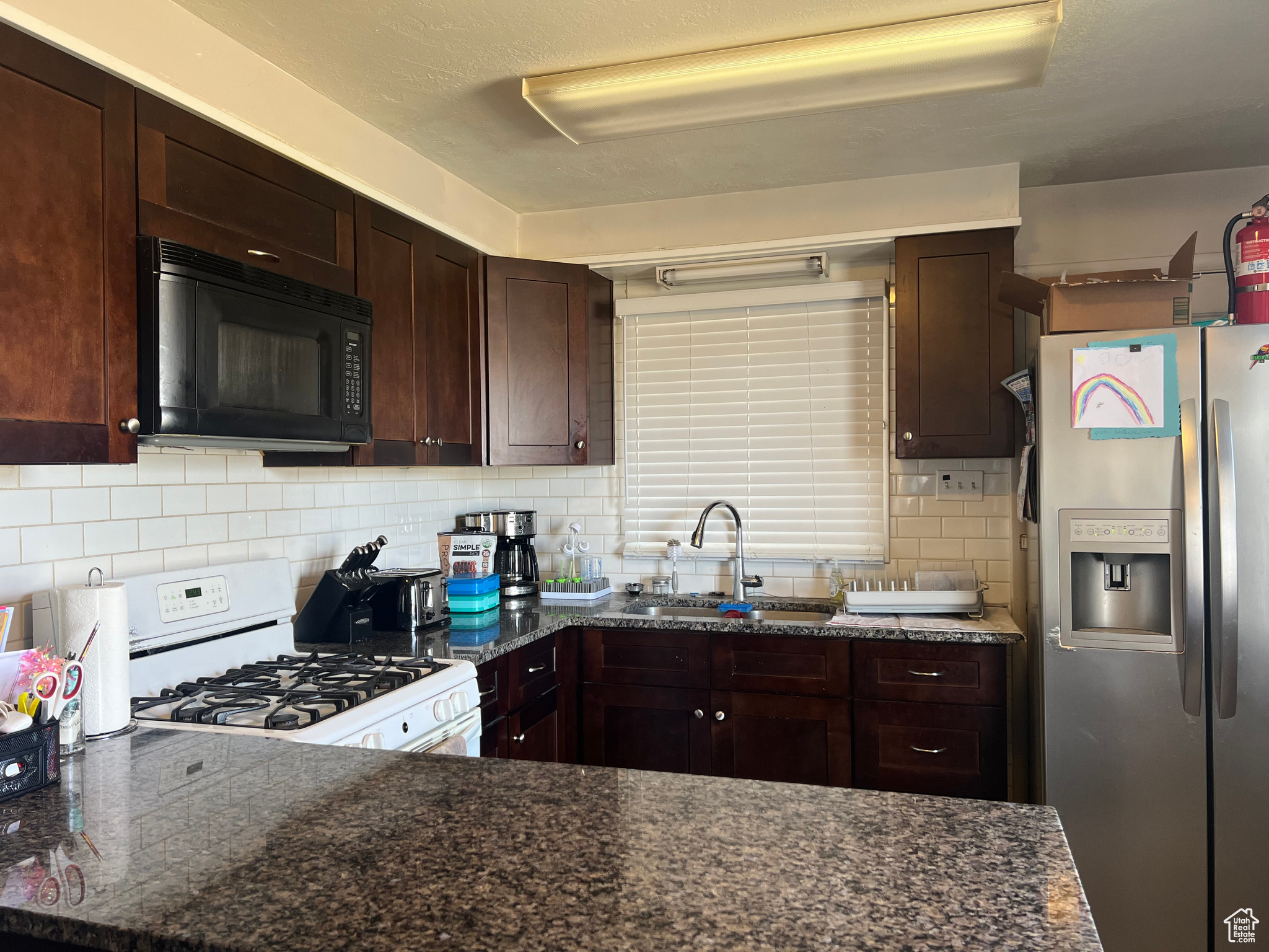 Kitchen featuring sink, stainless steel fridge, backsplash, and white gas range