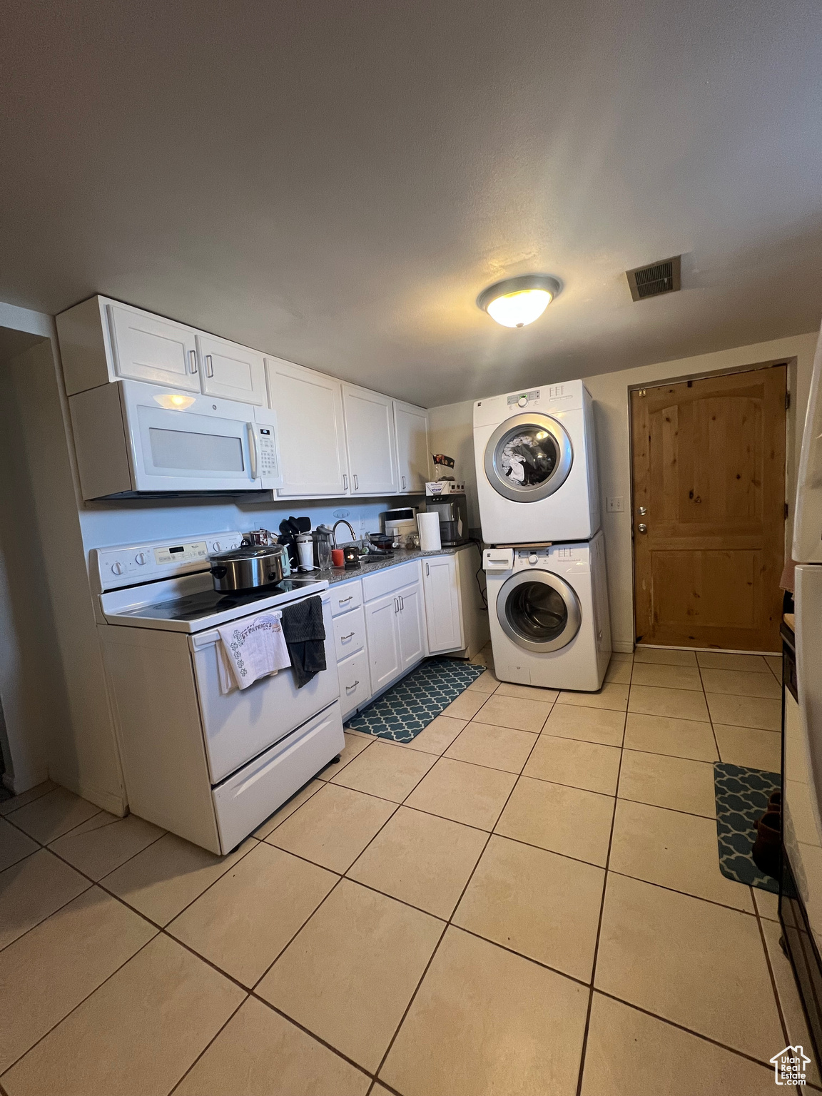 Kitchen with white appliances, light tile flooring, stacked washer and dryer, and white cabinets