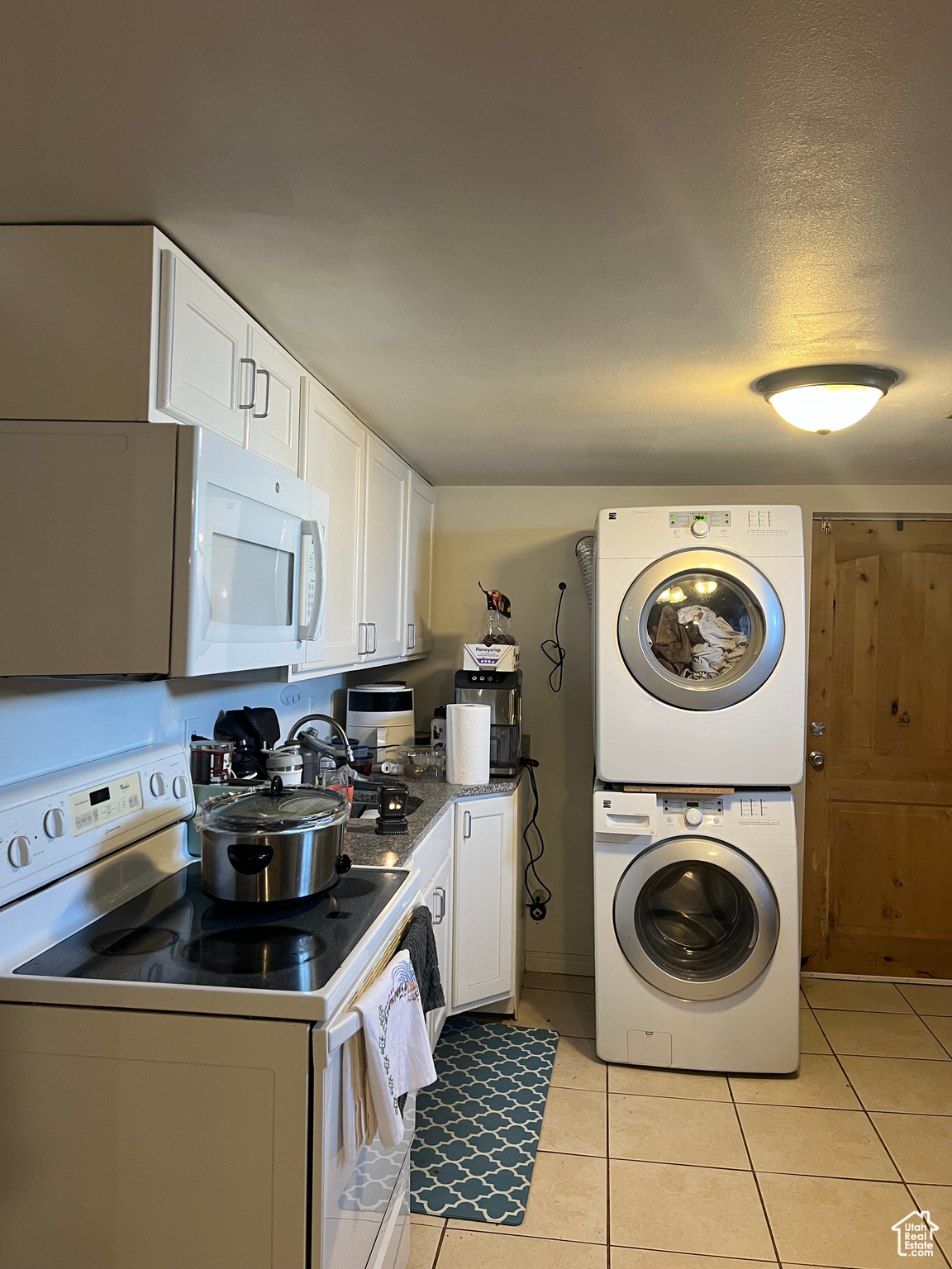 Kitchen featuring white cabinets, light tile flooring, stacked washer and clothes dryer, and electric range