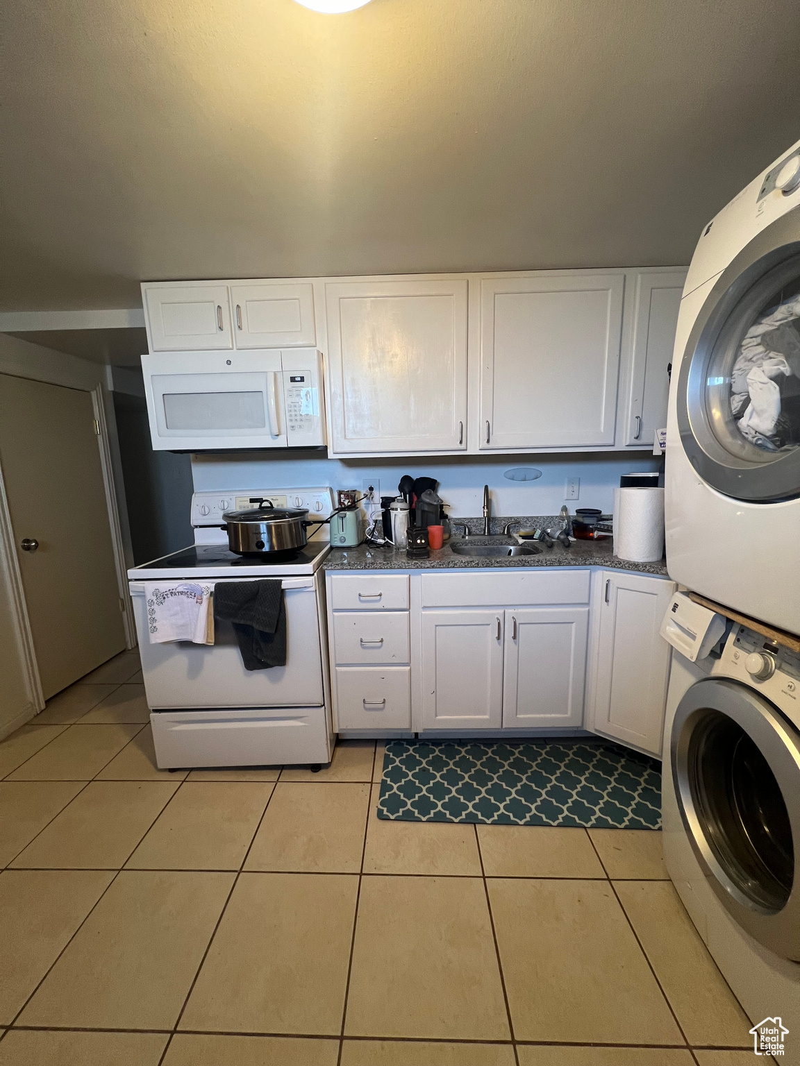 Kitchen featuring stacked washer / drying machine, white cabinets, light tile floors, and white appliances