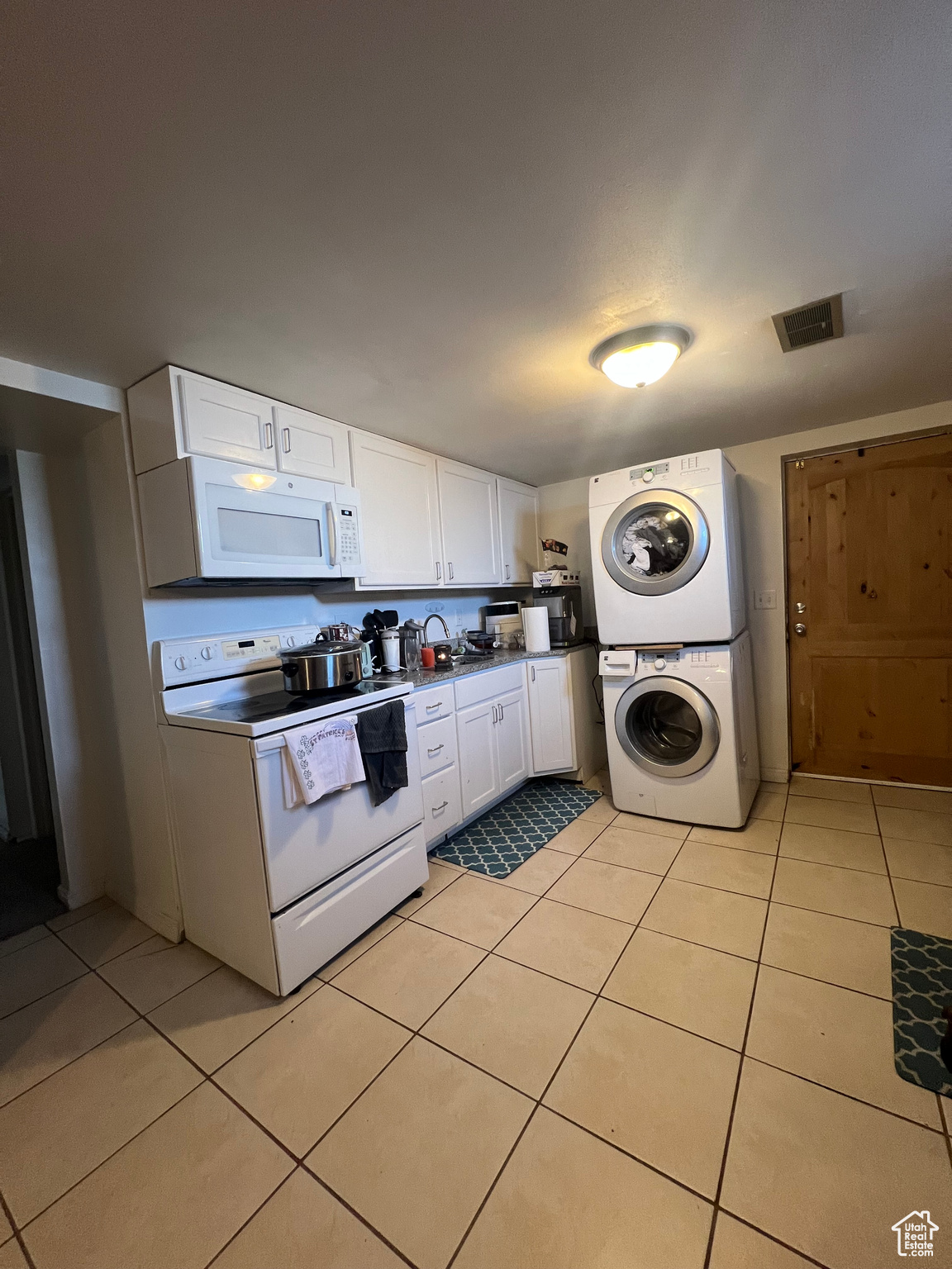 Kitchen with light tile floors, stacked washer and dryer, white cabinetry, and white appliances