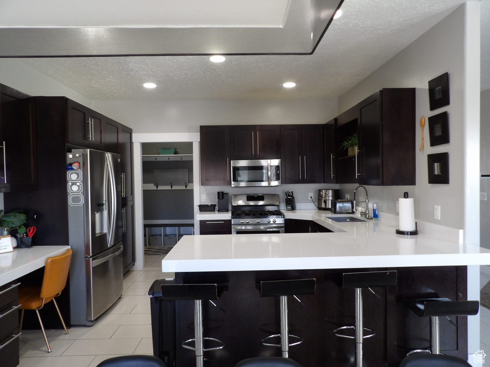 Kitchen with dark brown cabinets, light tile flooring, stainless steel appliances, a breakfast bar area, and sink
