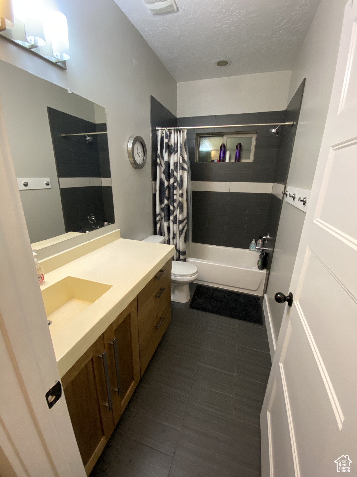 Full bathroom featuring a textured ceiling, vanity, shower / bath combination with curtain, toilet, and tile flooring