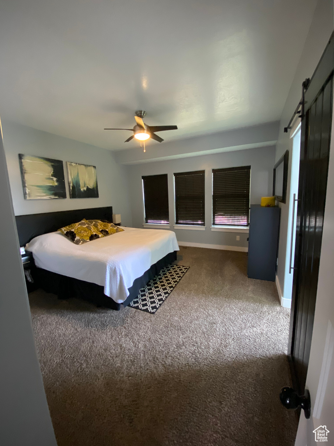 Bedroom featuring dark colored carpet, ceiling fan, and a barn door