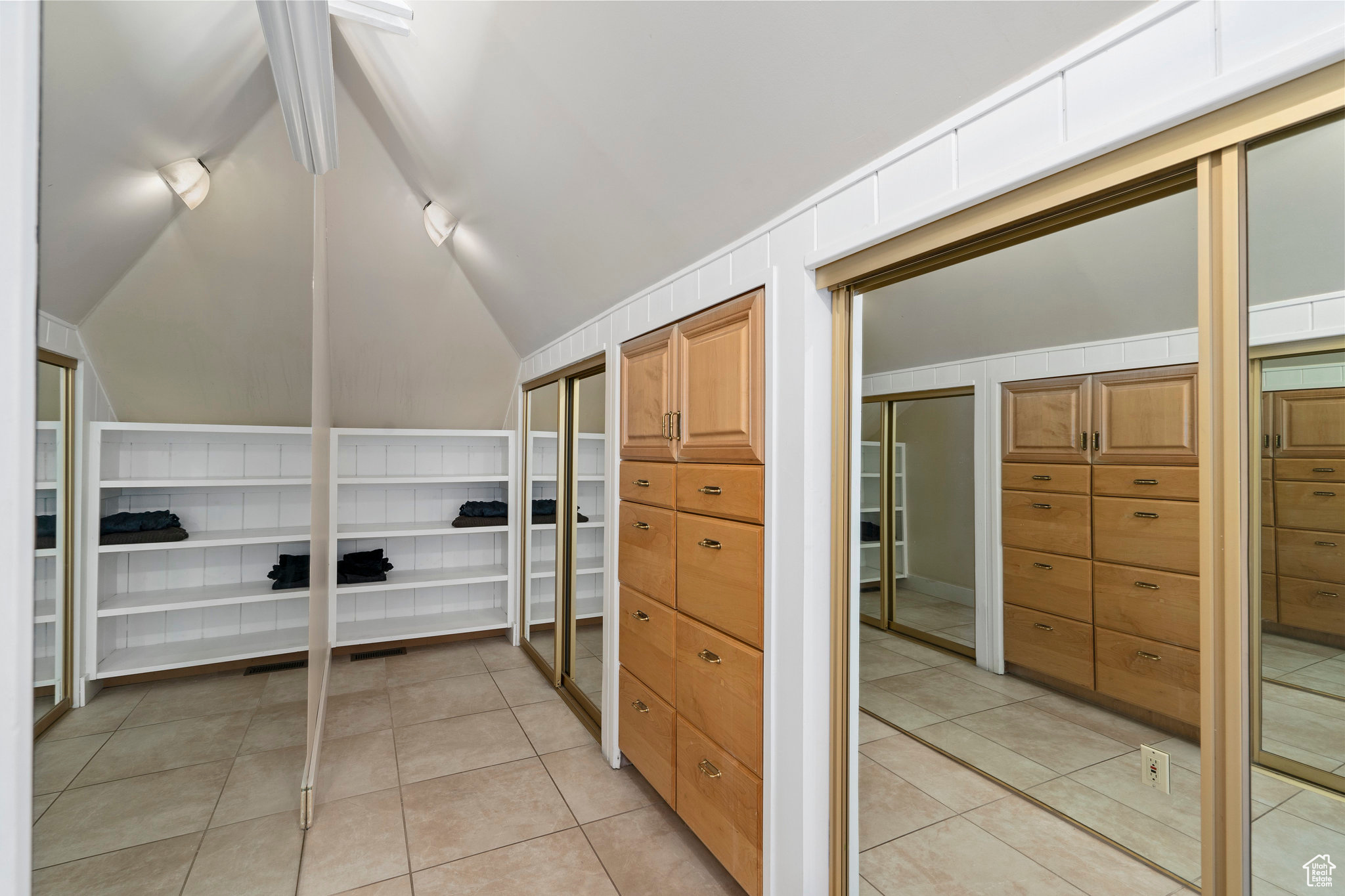 Master walk-in closet with lofted ceiling and light tile floors as part of the master bathroom.