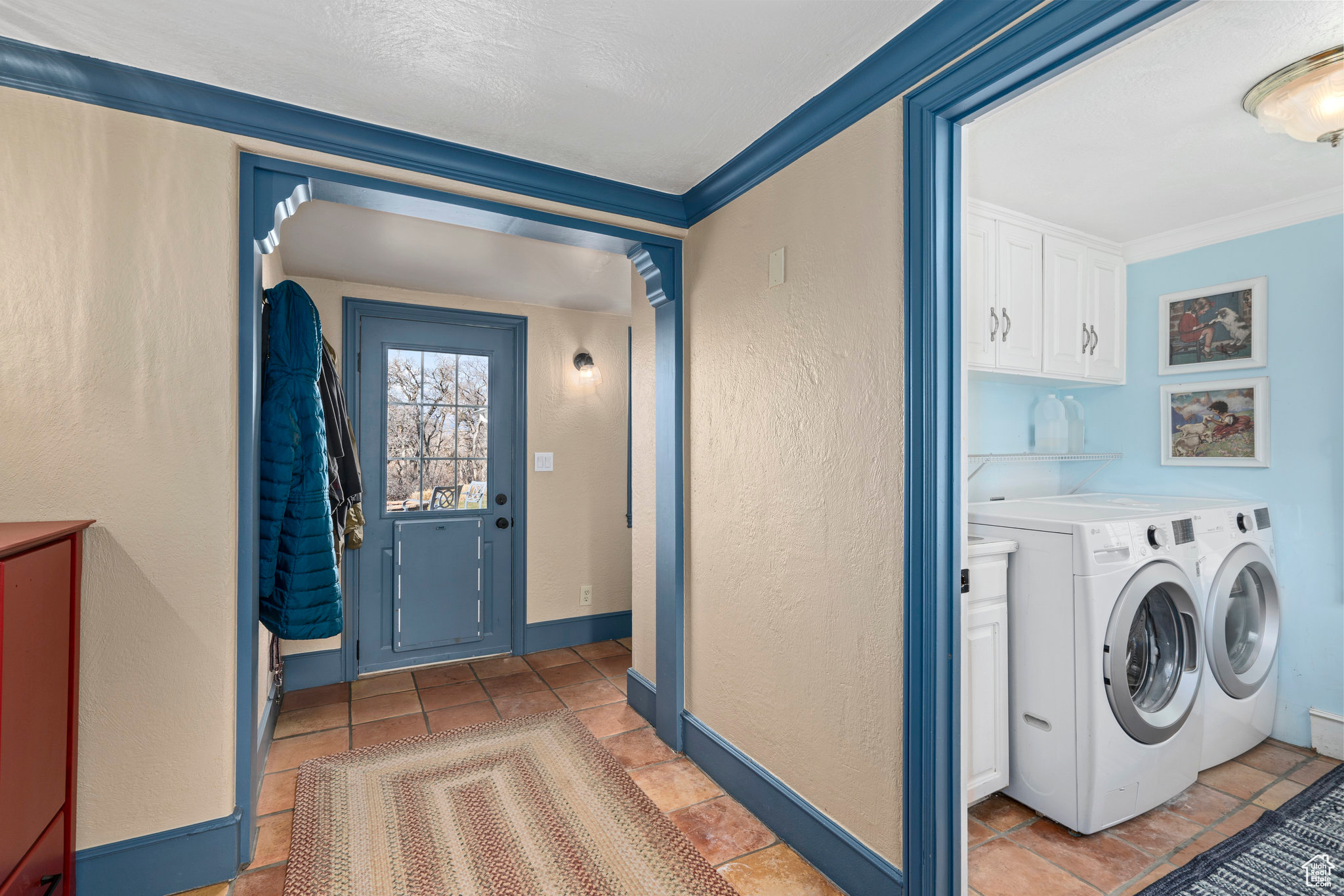 Clothes washing area with washer and clothes dryer, light tile floors, crown molding, and cabinets, tiled entryway between garage, kitchen, front and back yards.