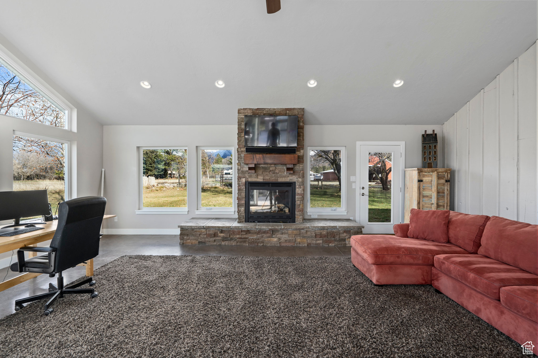 Office space with a stone fireplace, ceiling fan, and vaulted ceiling. Enjoy close to 600 square feet of entertaining or gathering space in this cozy sunroom behind the garage on the north side of the home.
