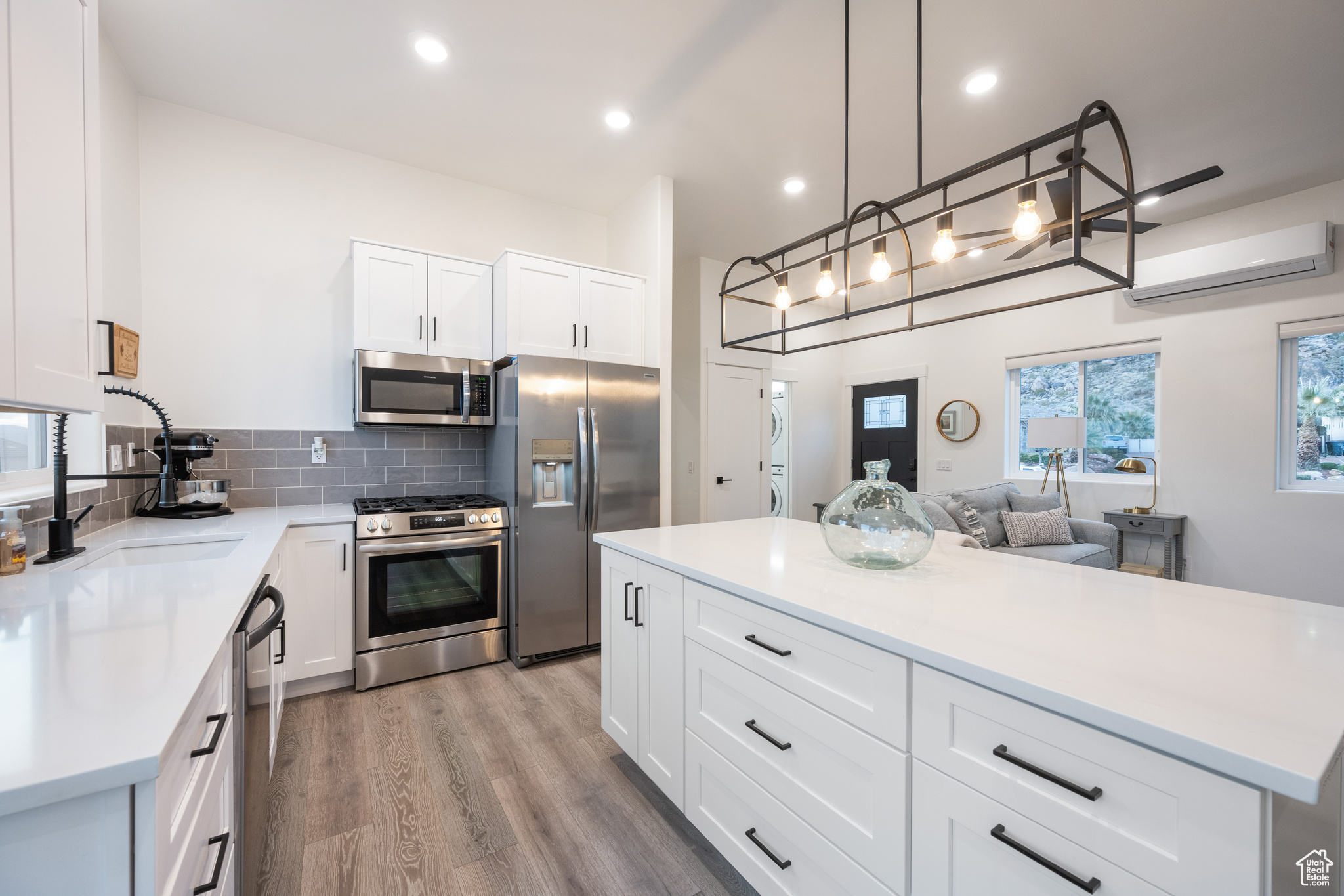 Kitchen featuring stainless steel appliances, white cabinetry, light hardwood / wood-style floors, and a wall unit AC