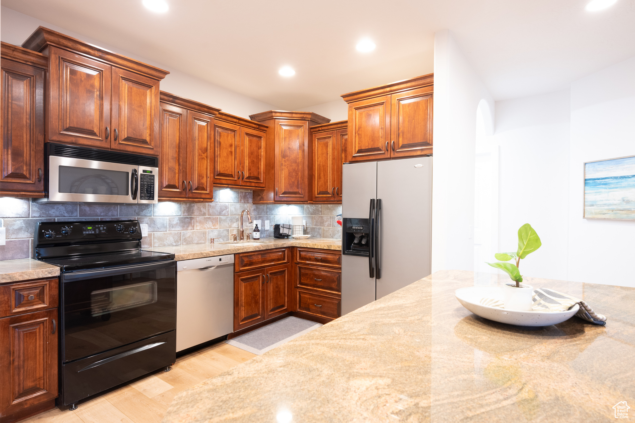 Kitchen featuring stainless steel appliances, light stone countertops, tasteful backsplash, light hardwood / wood-style flooring, and sink