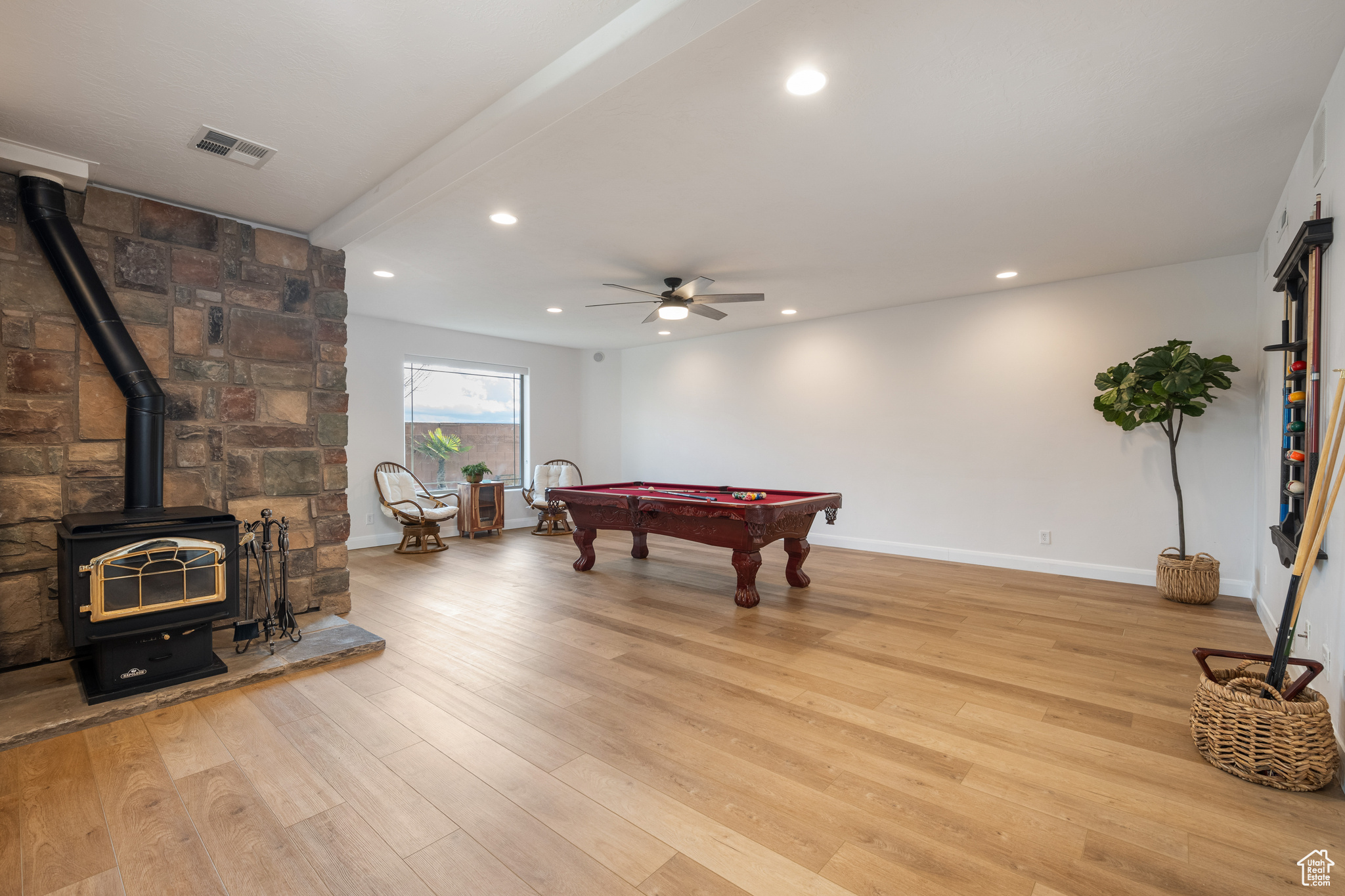 Rec room with light wood-type flooring, ceiling fan, a wood stove, beamed ceiling, and billiards