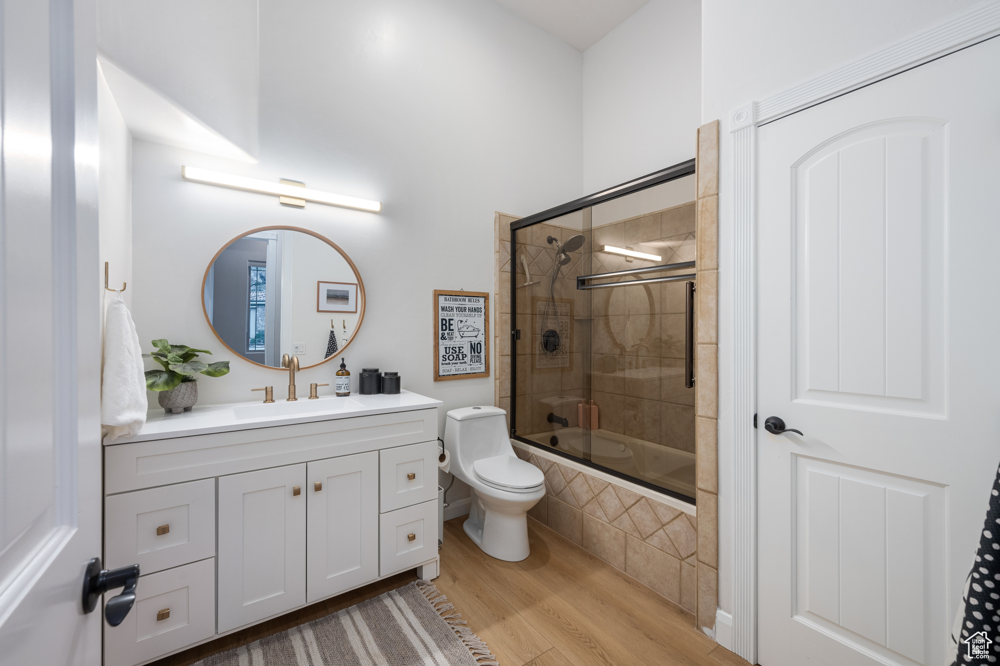 Full bathroom with vanity, toilet, bath / shower combo with glass door, and wood-type flooring