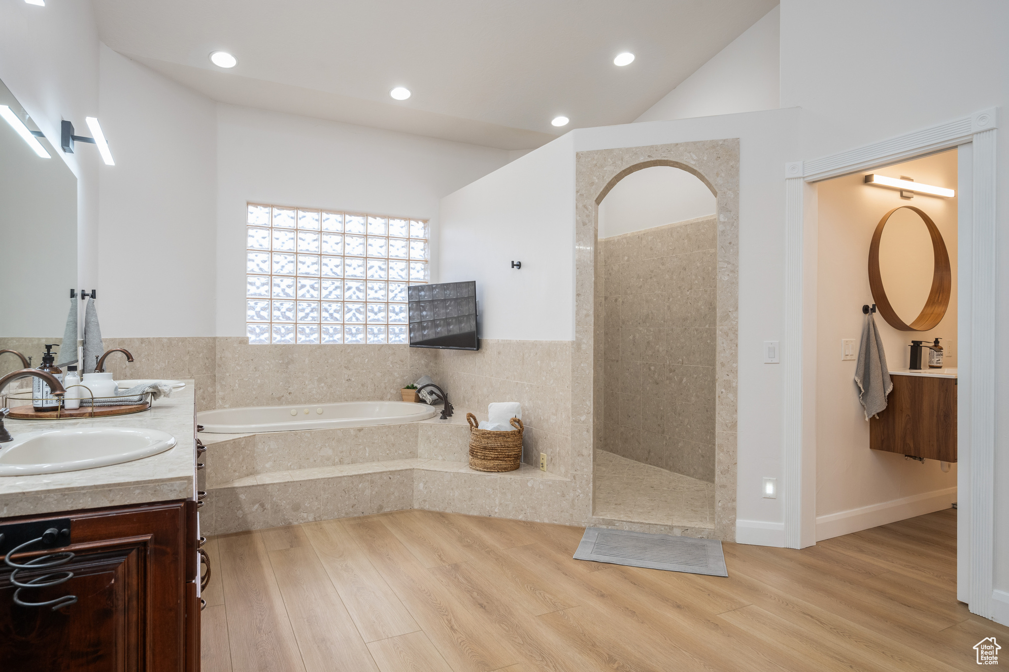 Bathroom with dual bowl vanity, hardwood / wood-style flooring, lofted ceiling, and tiled bath