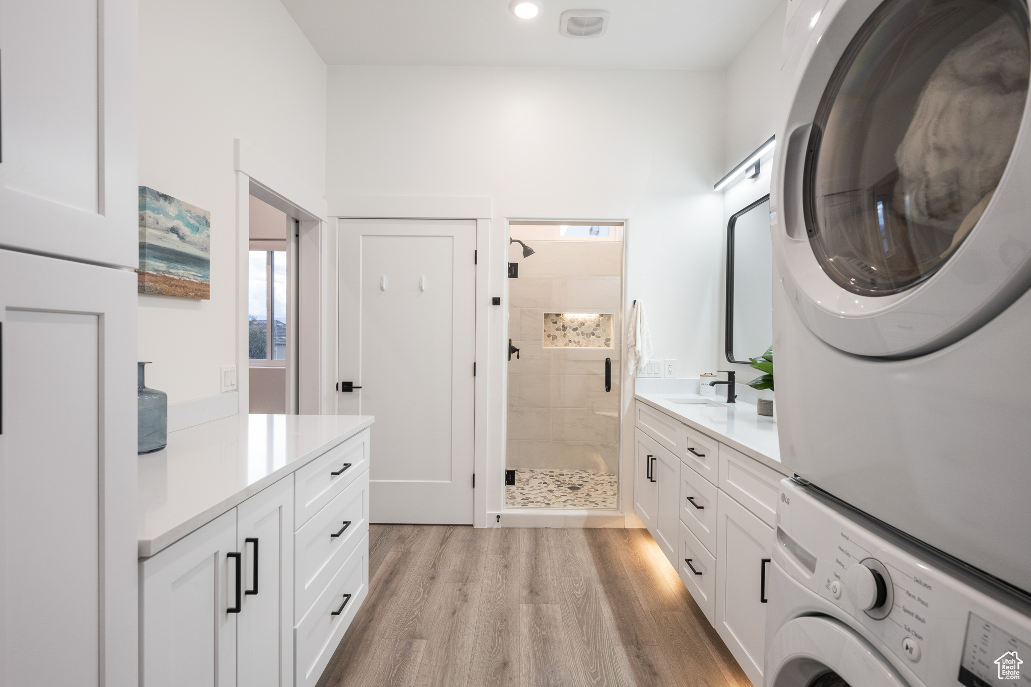 Interior space featuring vanity, a tile shower, hardwood / wood-style floors, and stacked washer / dryer