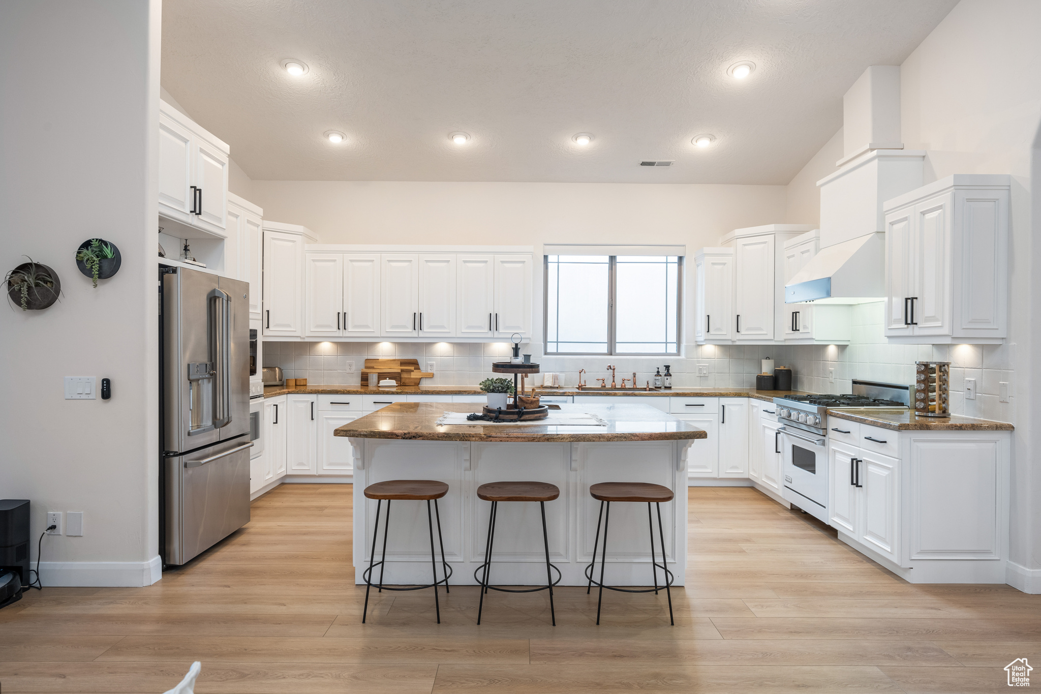 Kitchen with white cabinetry, a kitchen island, a breakfast bar area, backsplash, and high quality appliances