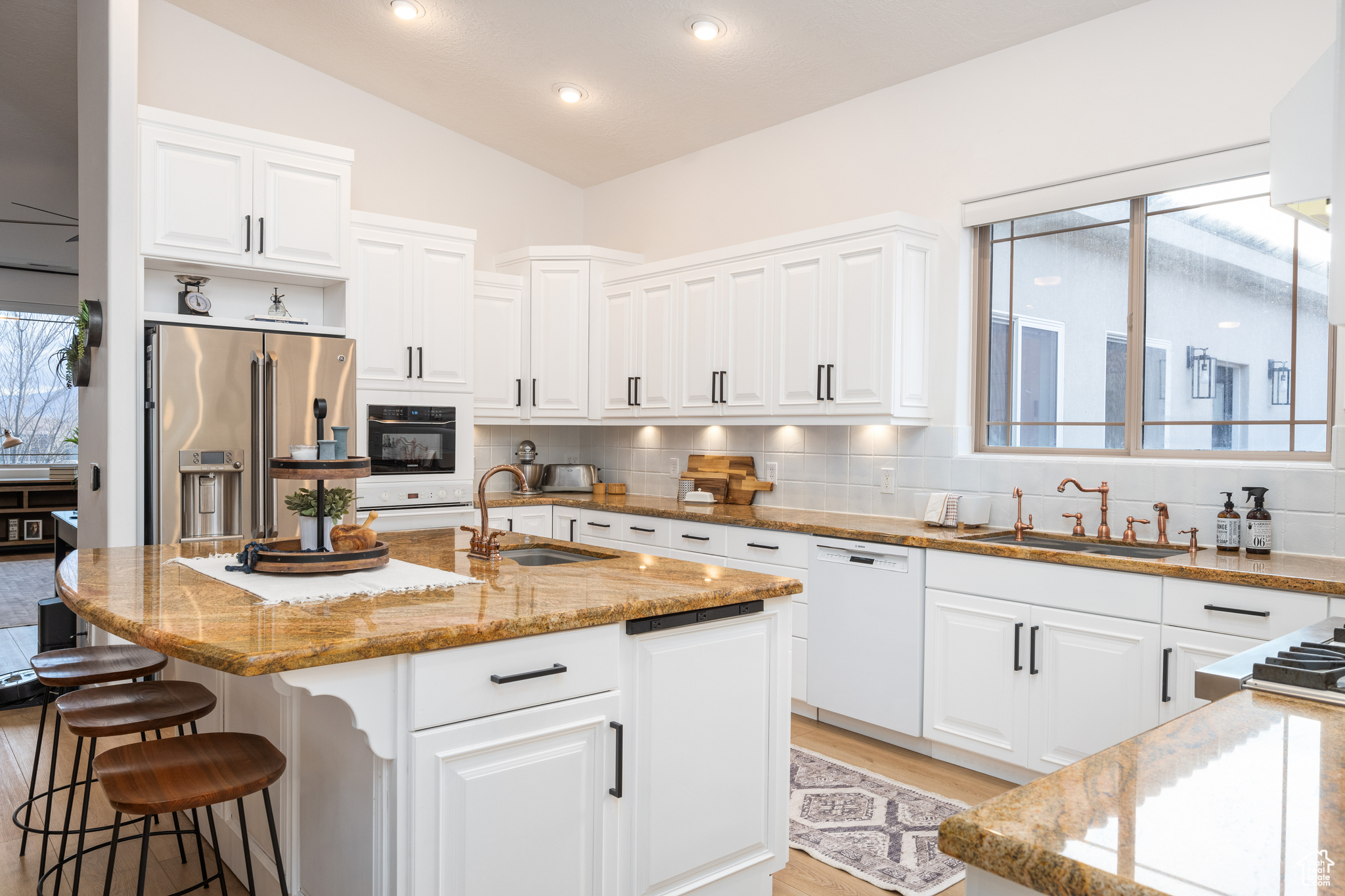 Kitchen featuring dishwasher, a center island with sink, lofted ceiling, high quality fridge, and tasteful backsplash