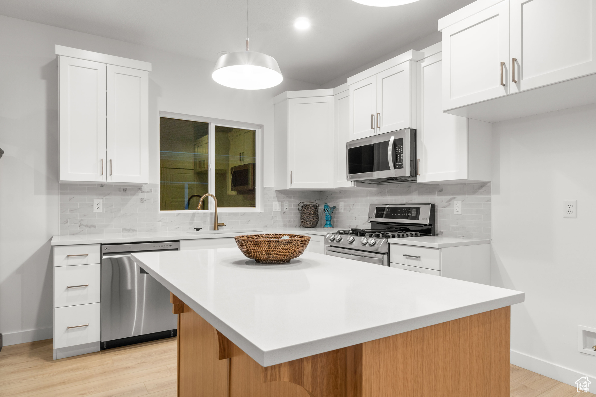 Kitchen featuring appliances with stainless steel finishes, a center island, backsplash, and white cabinetry