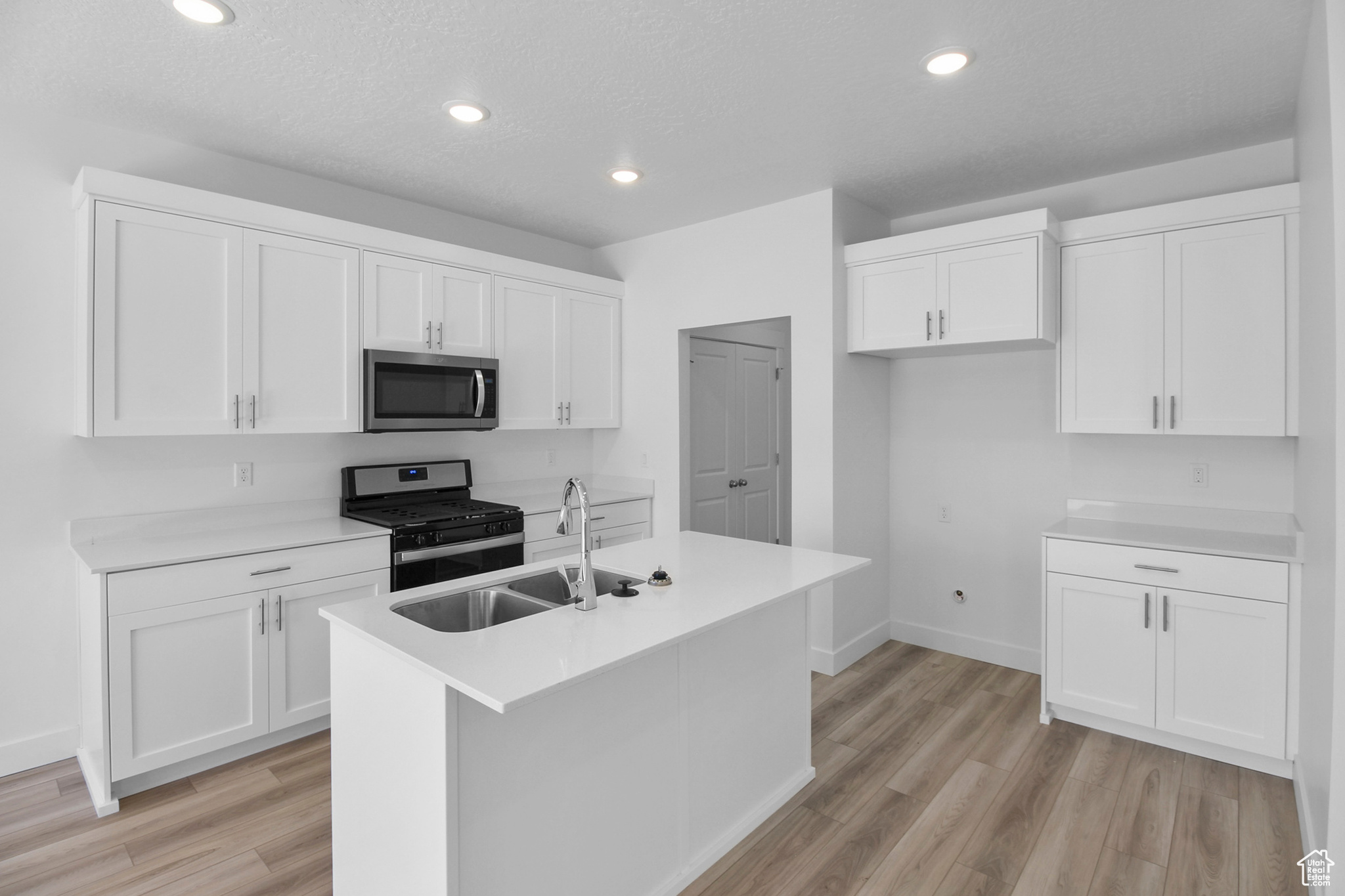 Kitchen featuring white cabinetry, a center island with sink, appliances with stainless steel finishes, light hardwood / wood-style flooring, and sink