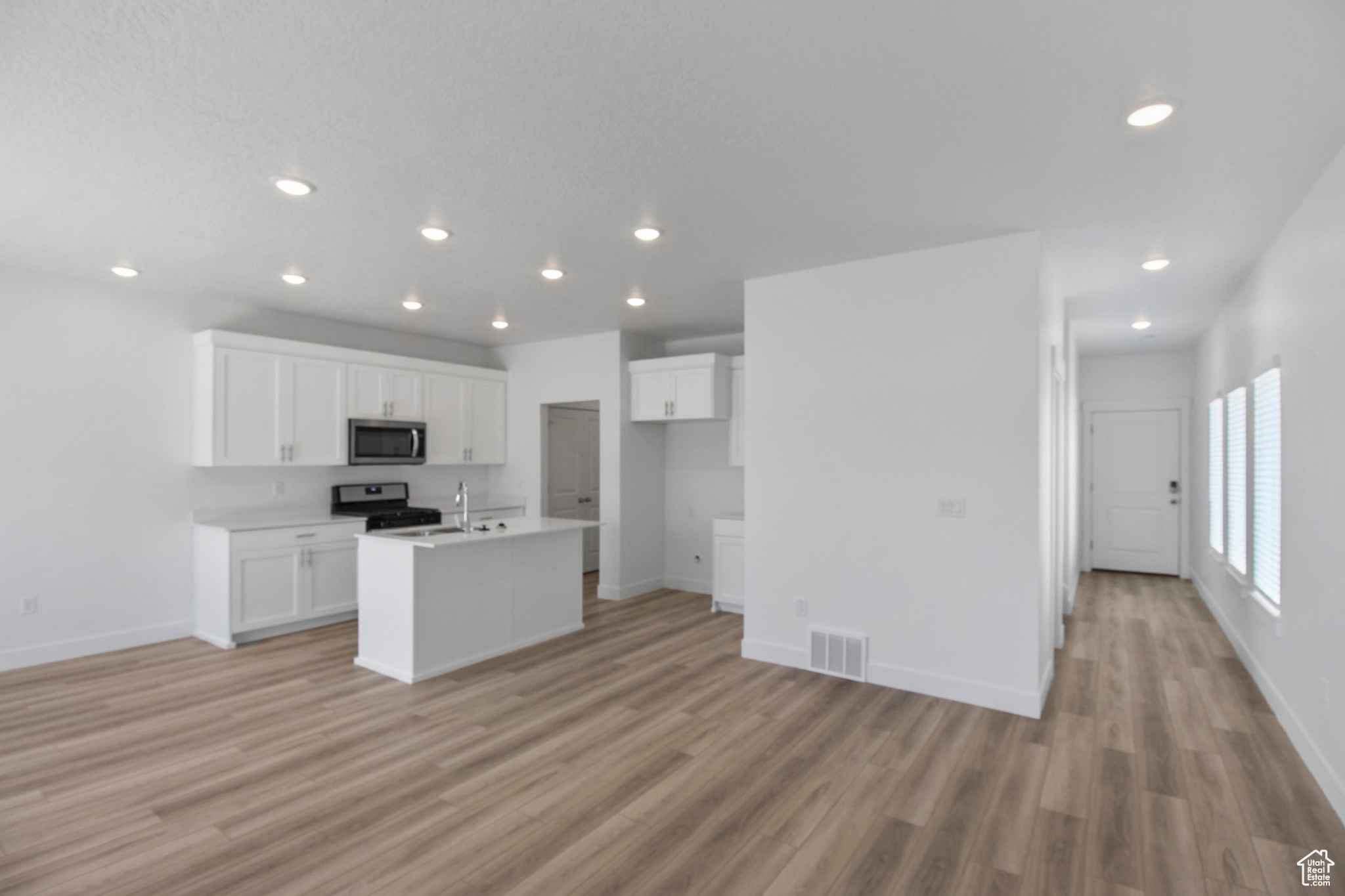 Living Room, Dining Room, and Kitchen with appliances with stainless steel finishes, light hardwood / wood-style flooring, a kitchen island with sink, and white cabinetry *Photo is of a previously build home. Listed Home is not an end unit. No windows in
