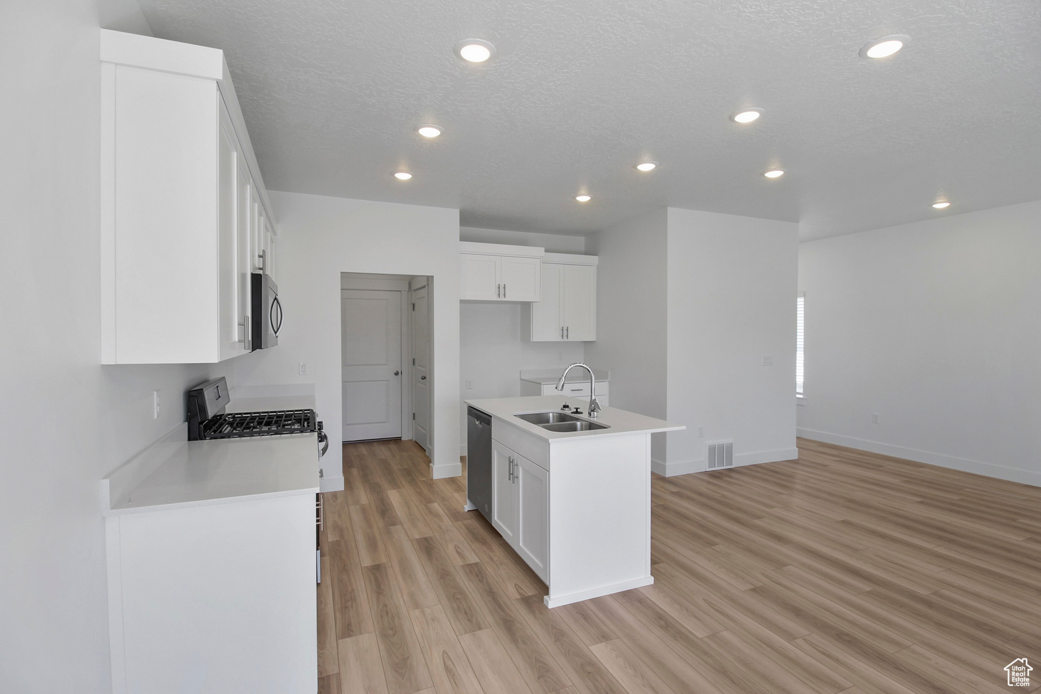 Kitchen with light wood-type flooring, white cabinets, sink, an island with sink, and stainless steel appliances