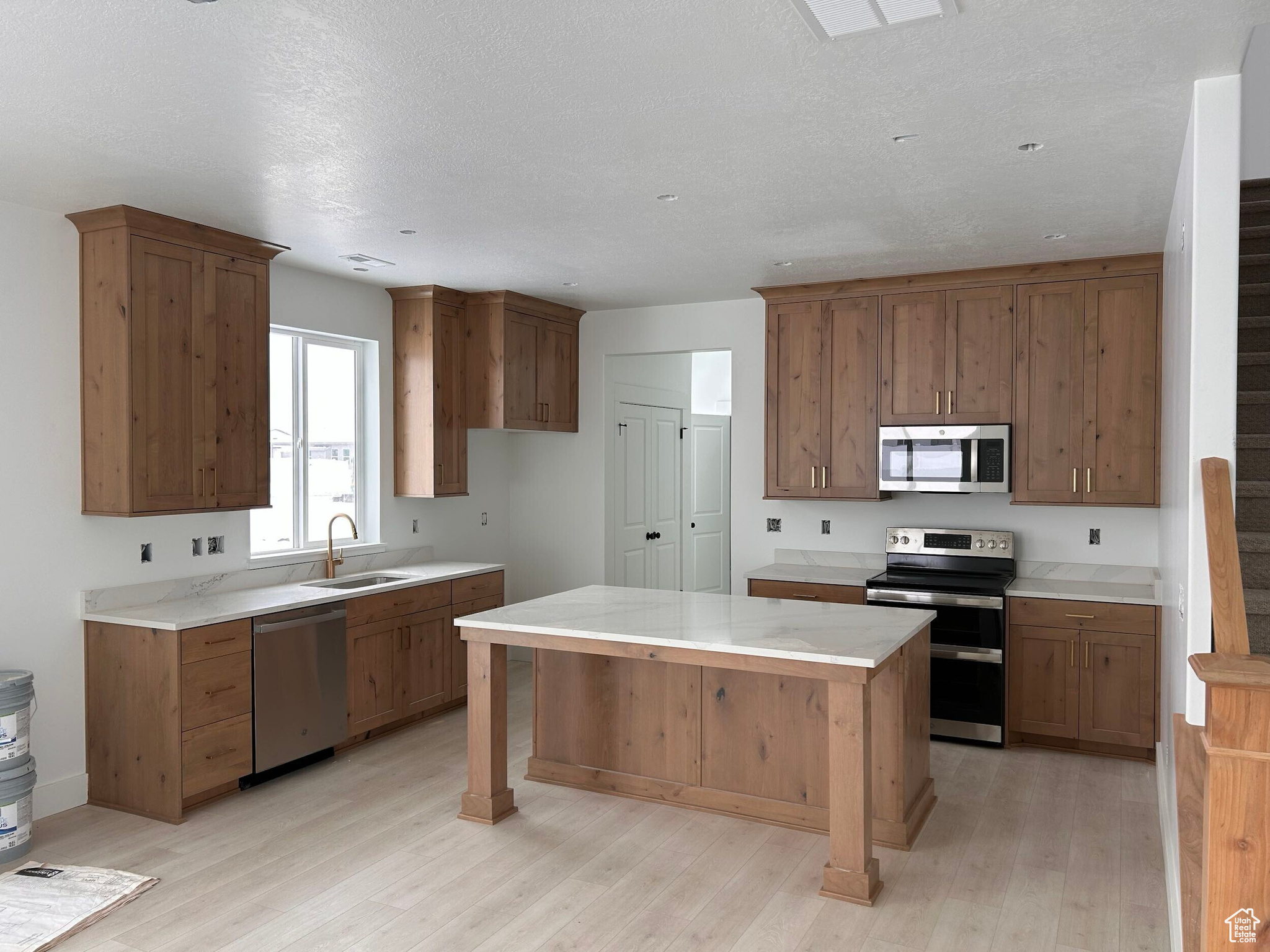 Kitchen with appliances with stainless steel finishes, sink, a textured ceiling, and light hardwood / wood-style floors