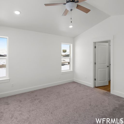Carpeted spare room with ceiling fan, a healthy amount of sunlight, and lofted ceiling