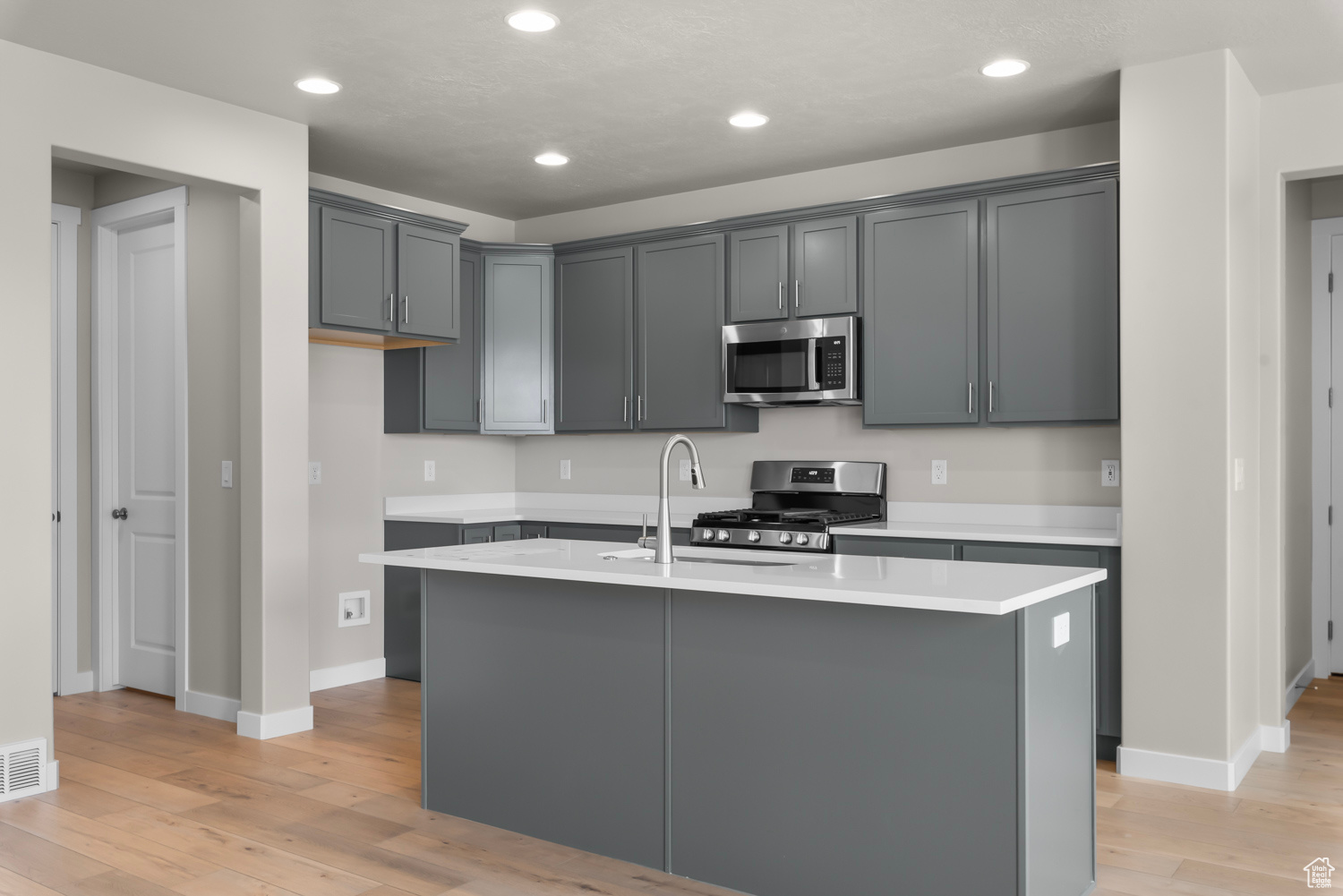 Kitchen with a kitchen island with sink, light wood-type flooring, gray cabinets, appliances with stainless steel finishes, and sink