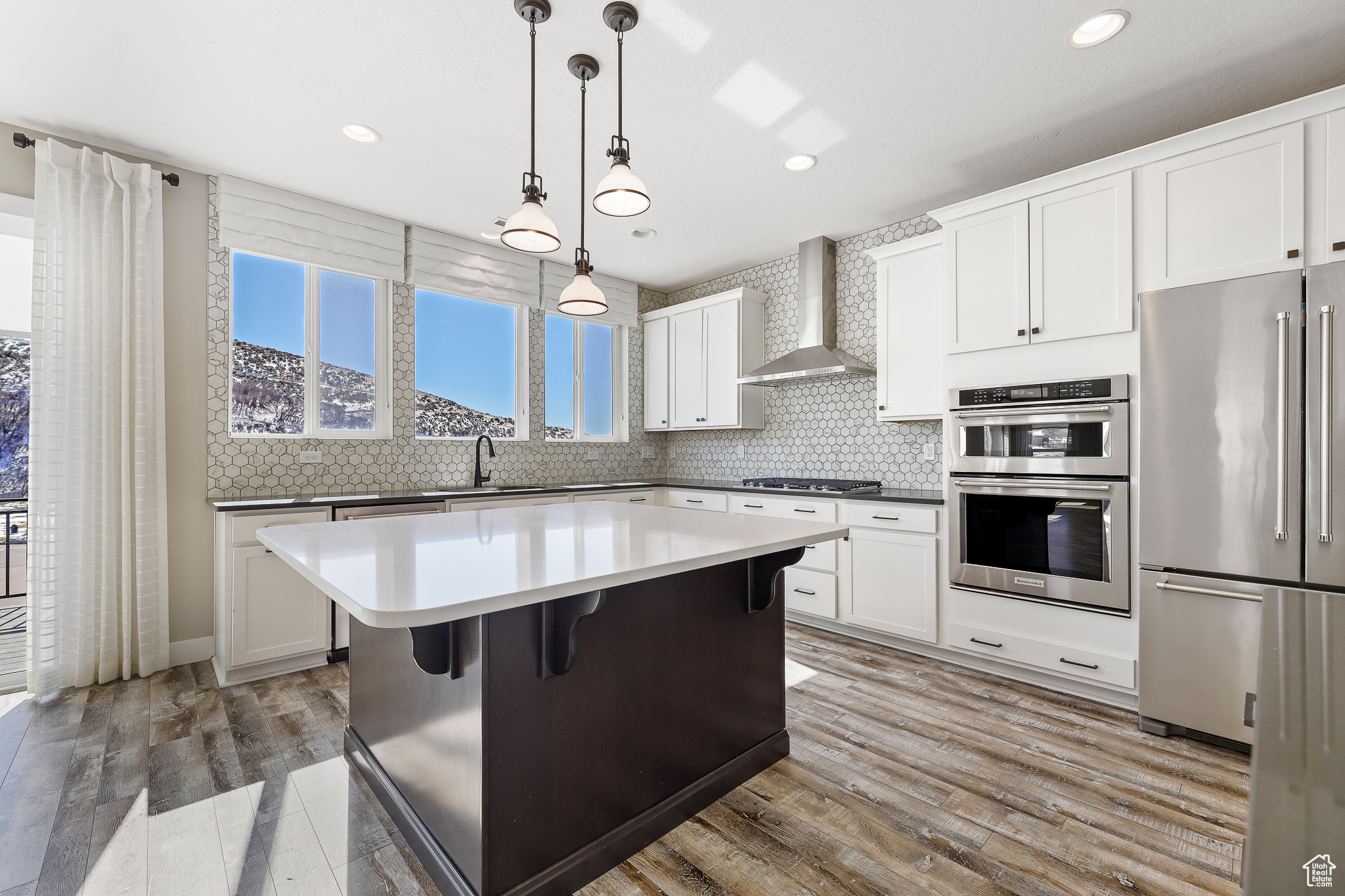 Kitchen featuring a kitchen island, wall chimney exhaust hood, appliances with stainless steel finishes, decorative light fixtures, and a breakfast bar area