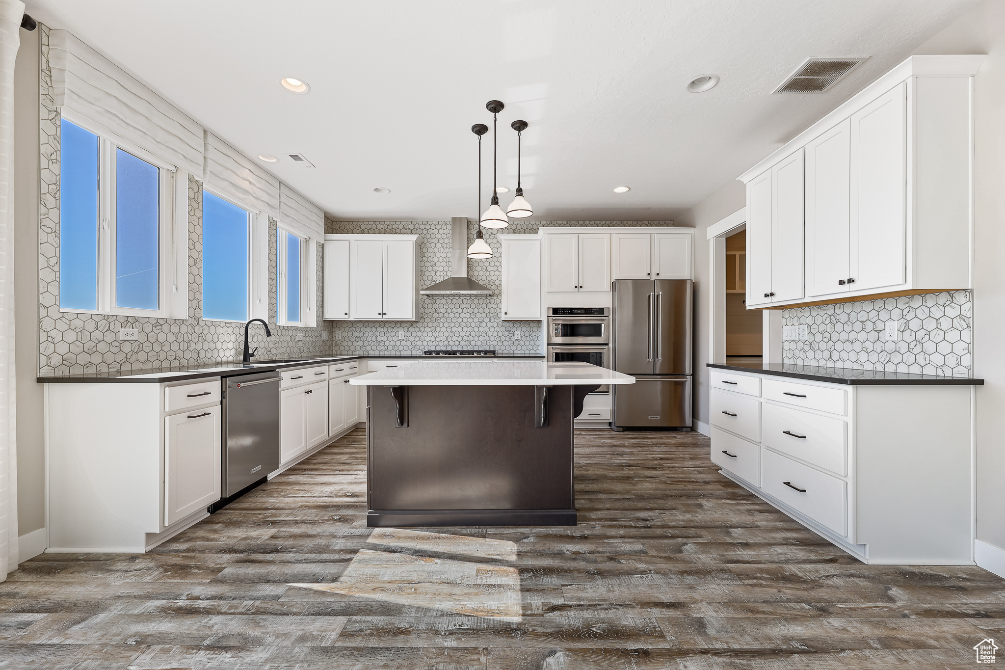 Kitchen with wall chimney range hood, appliances with stainless steel finishes, a kitchen breakfast bar, hanging light fixtures, and a center island