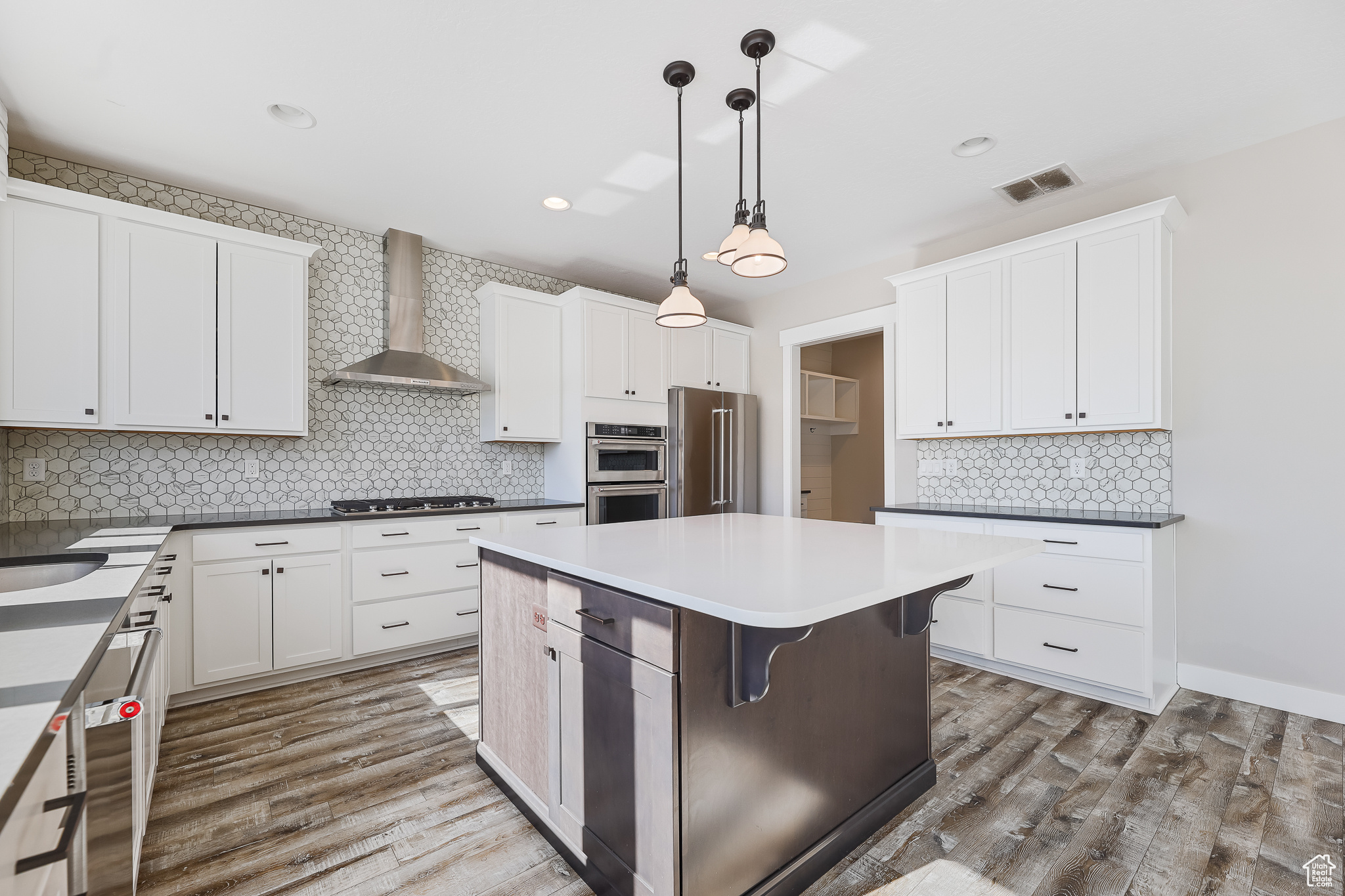 Kitchen featuring wall chimney range hood, pendant lighting, tasteful backsplash, a kitchen island, and stainless steel appliances