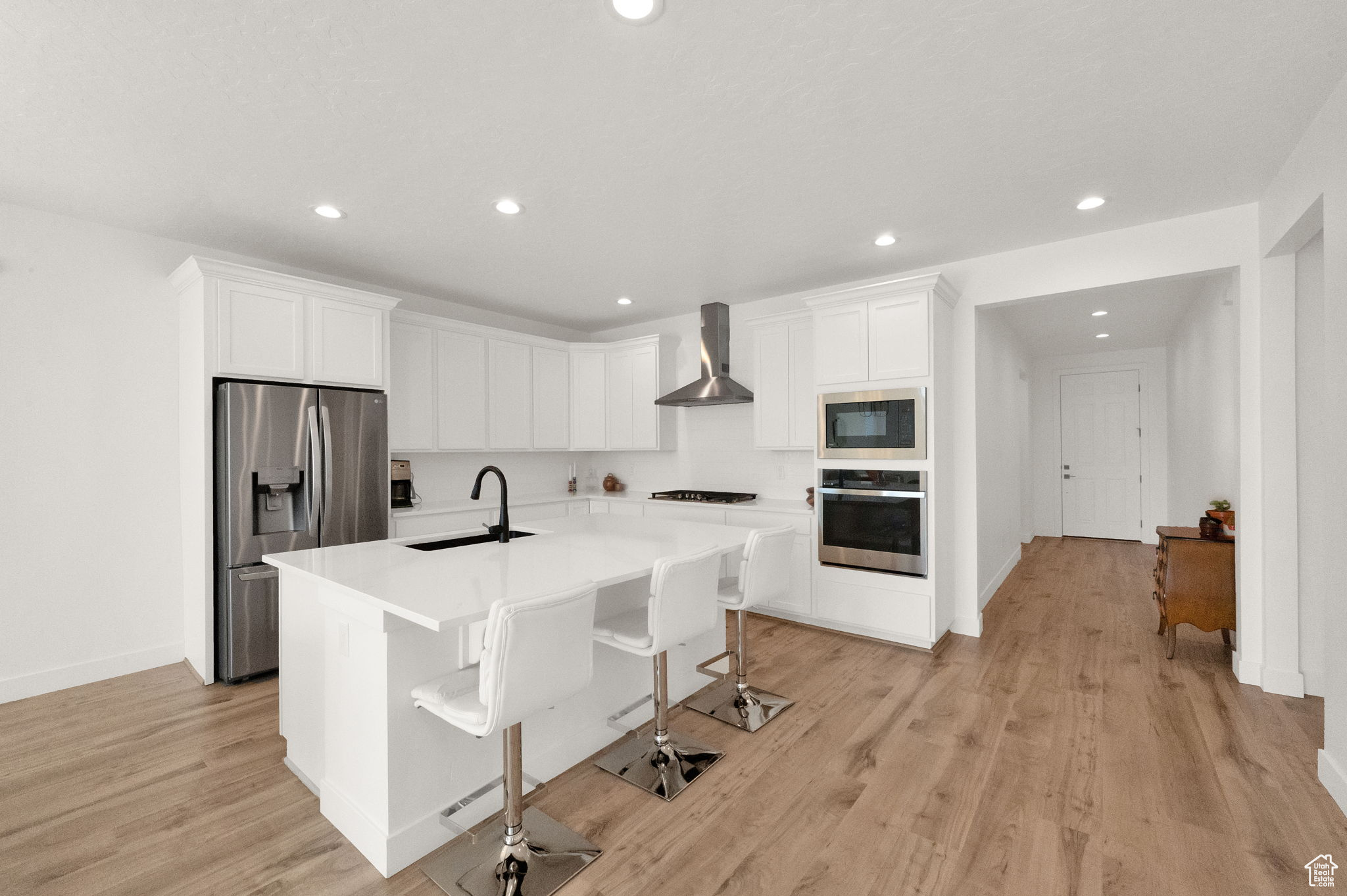 Kitchen featuring a kitchen island with sink, sink, light hardwood / wood-style floors, wall chimney exhaust hood, and appliances with stainless steel finishes